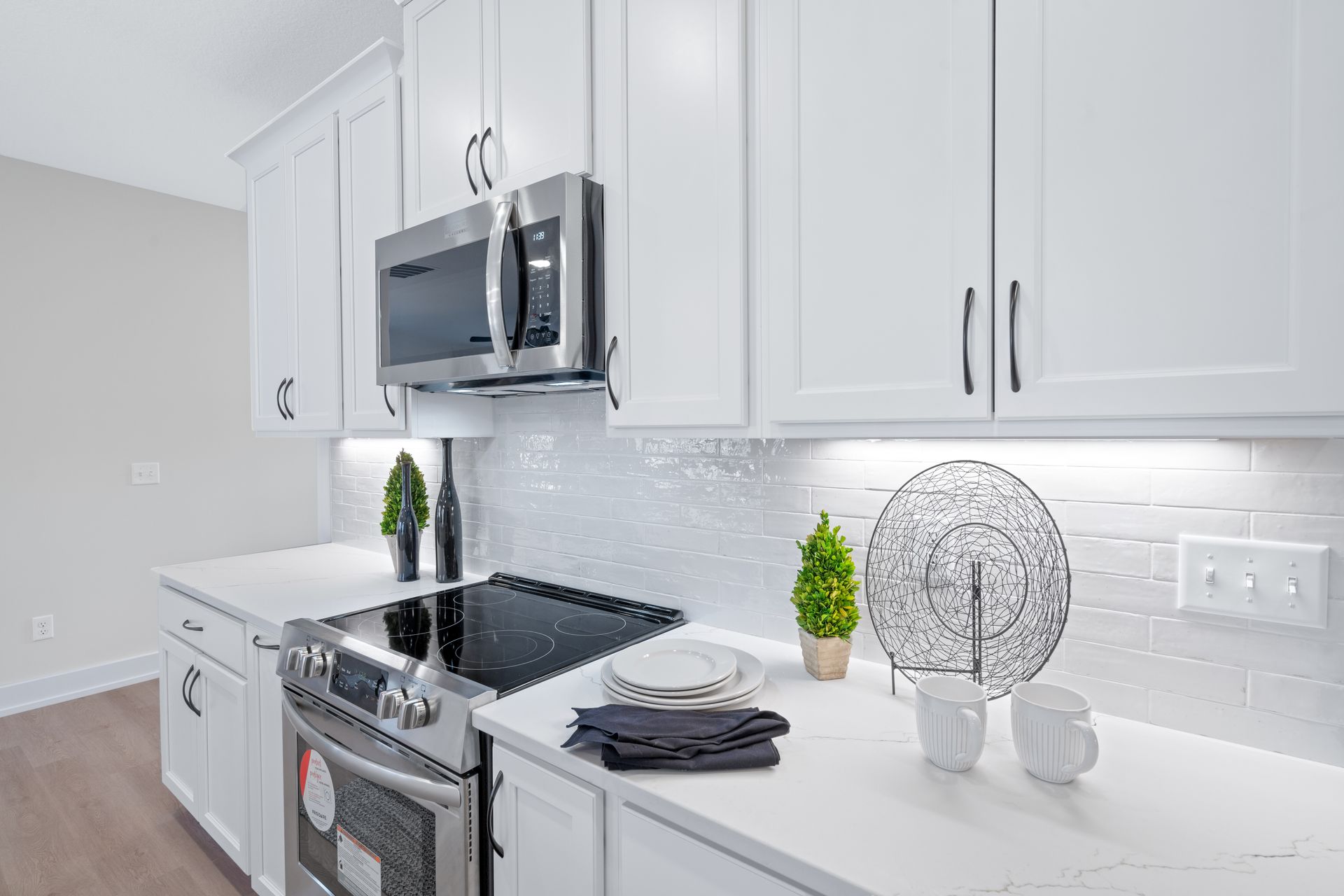 A kitchen with white cabinets , stainless steel appliances , a stove and a microwave.