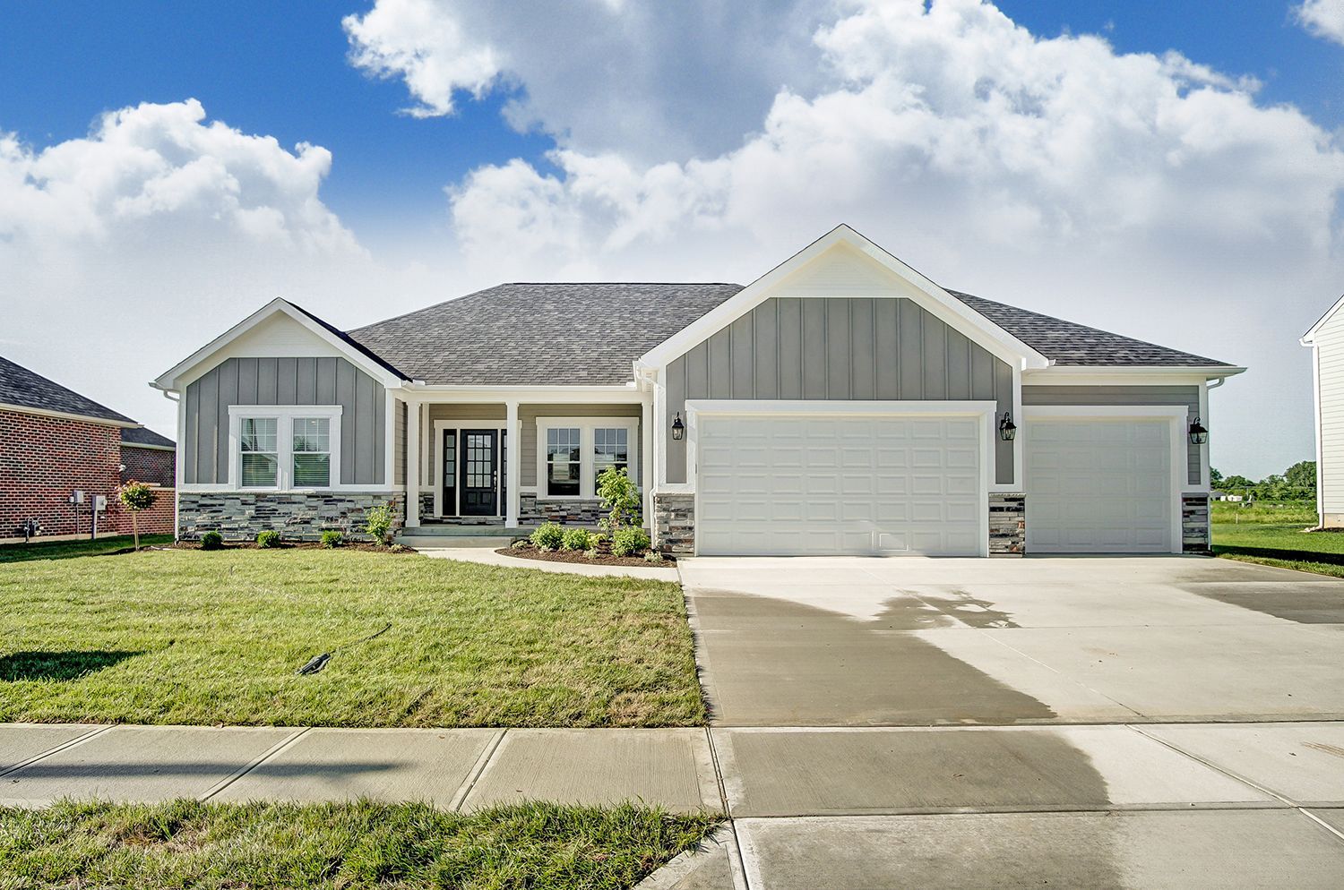 A gray and white house with a white garage door is sitting on top of a lush green field.
