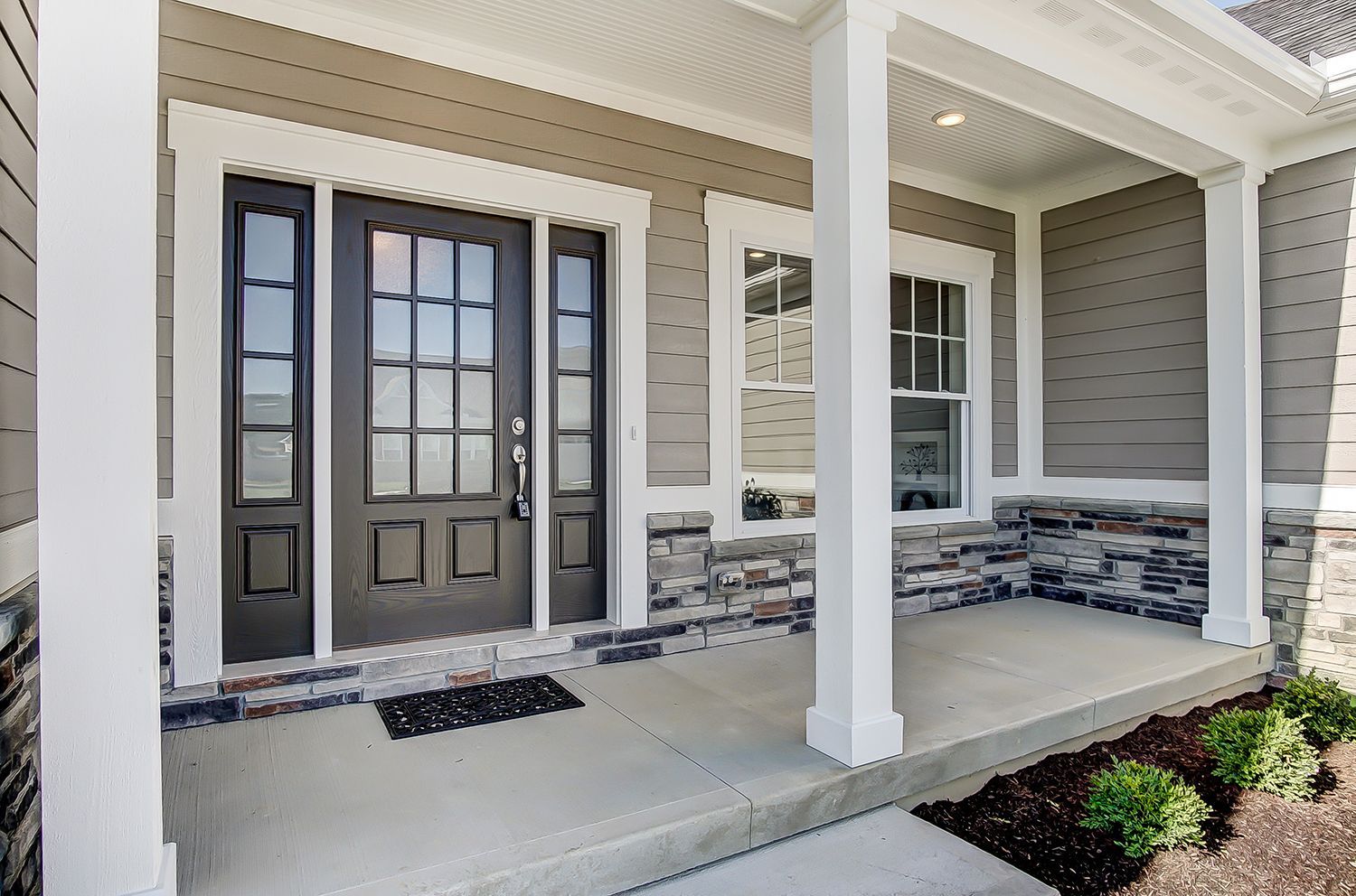 The front porch of a house with a porch and a black door.
