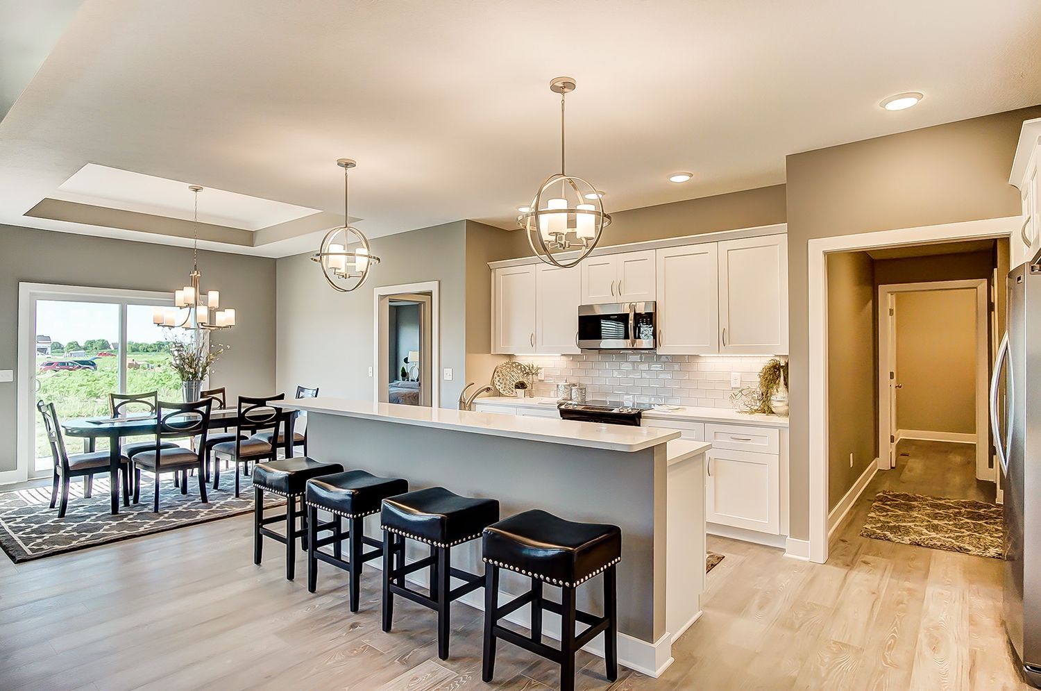 A kitchen with white cabinets , granite counter tops , stools and a dining room.