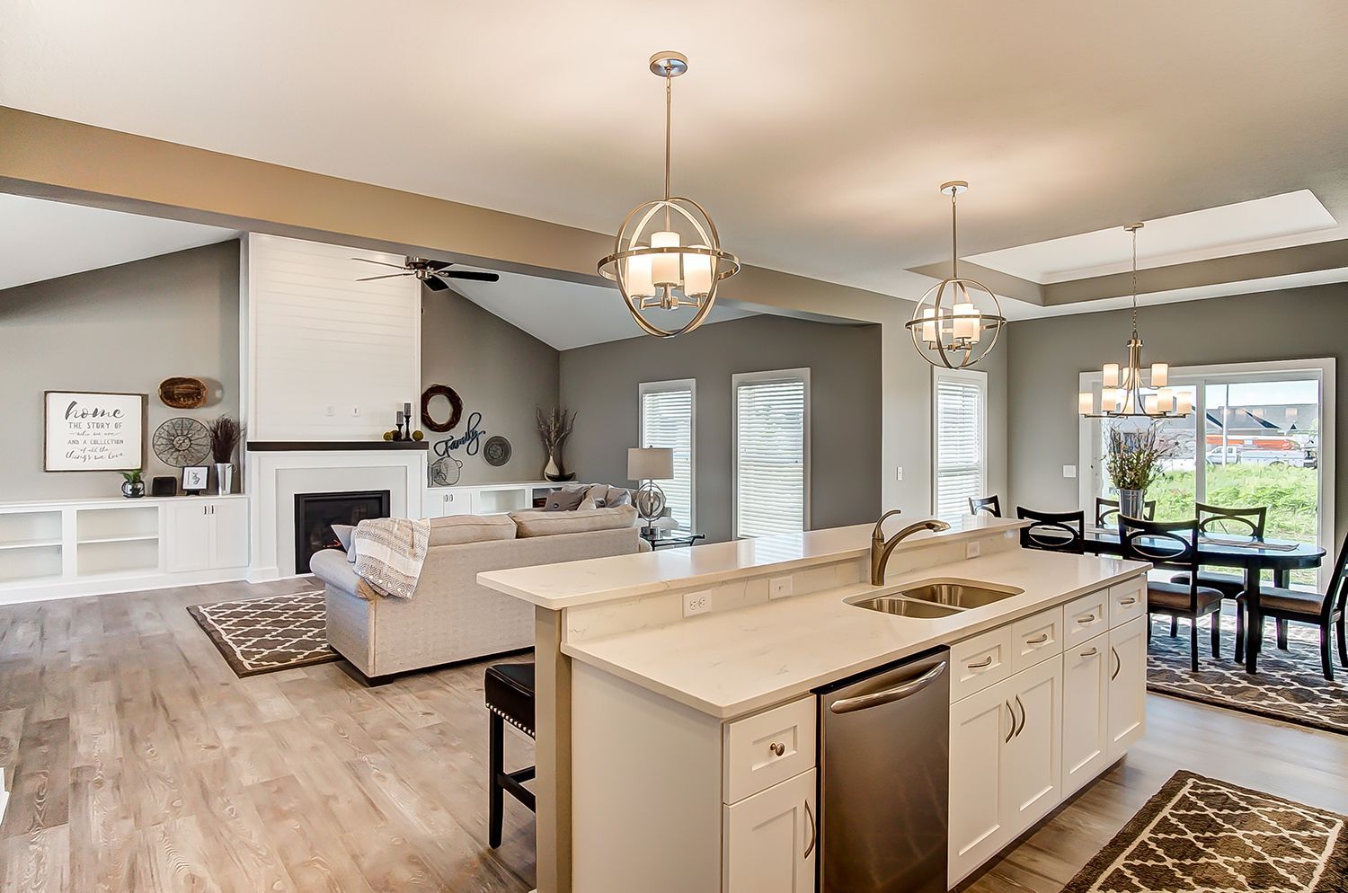A kitchen with a sink , dishwasher , and stainless steel appliances is open to a living room and dining room.