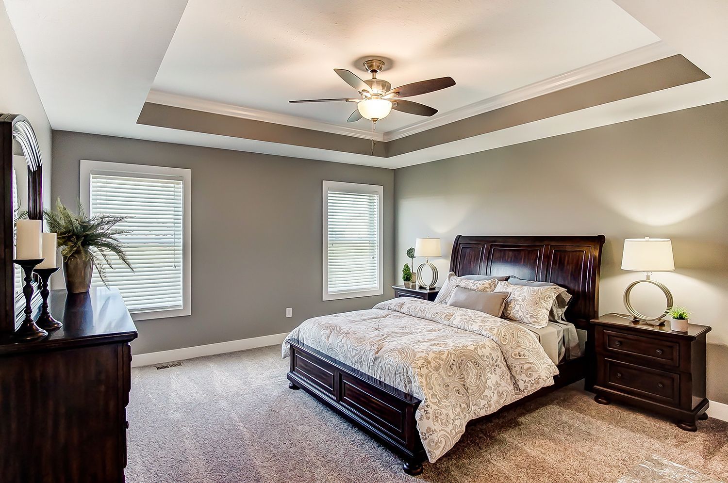 A bedroom with a bed , dresser , nightstand , mirror and ceiling fan.