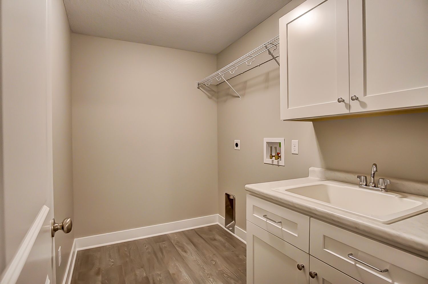 A laundry room with a sink , cabinets , and a clothes rack.
