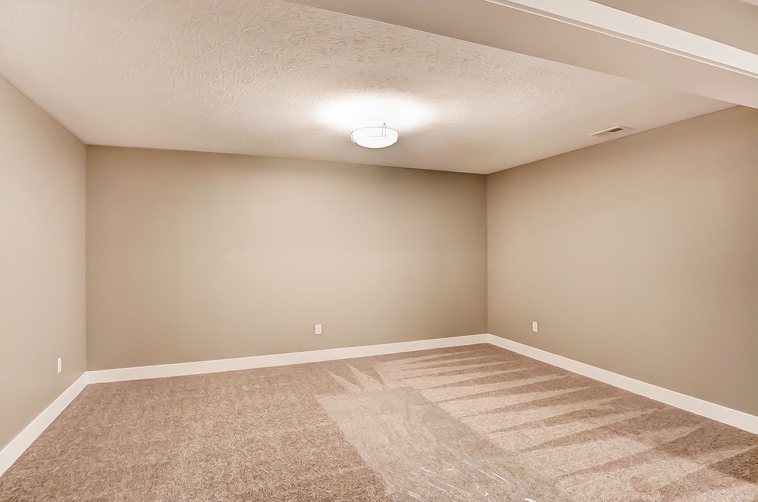 An empty basement with a carpeted floor and beige walls.