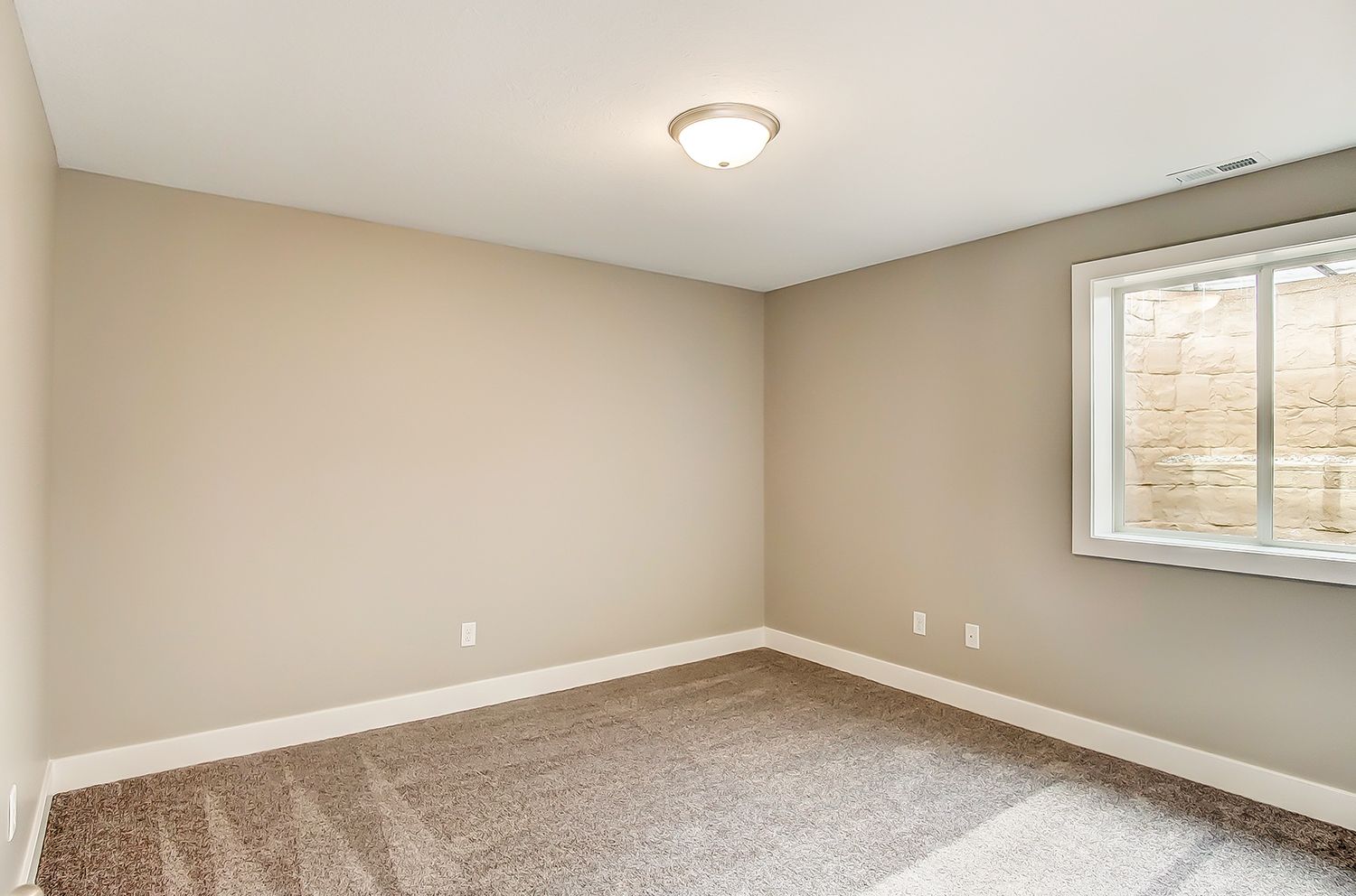 An empty bedroom with a window and a carpeted floor.