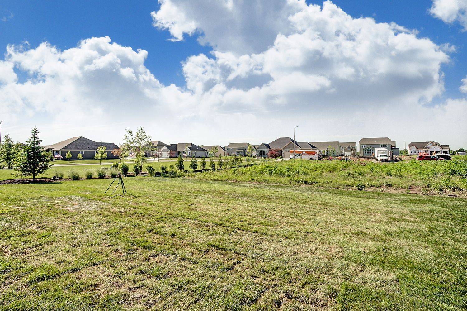 A large grassy field with houses in the background and a blue sky with clouds.