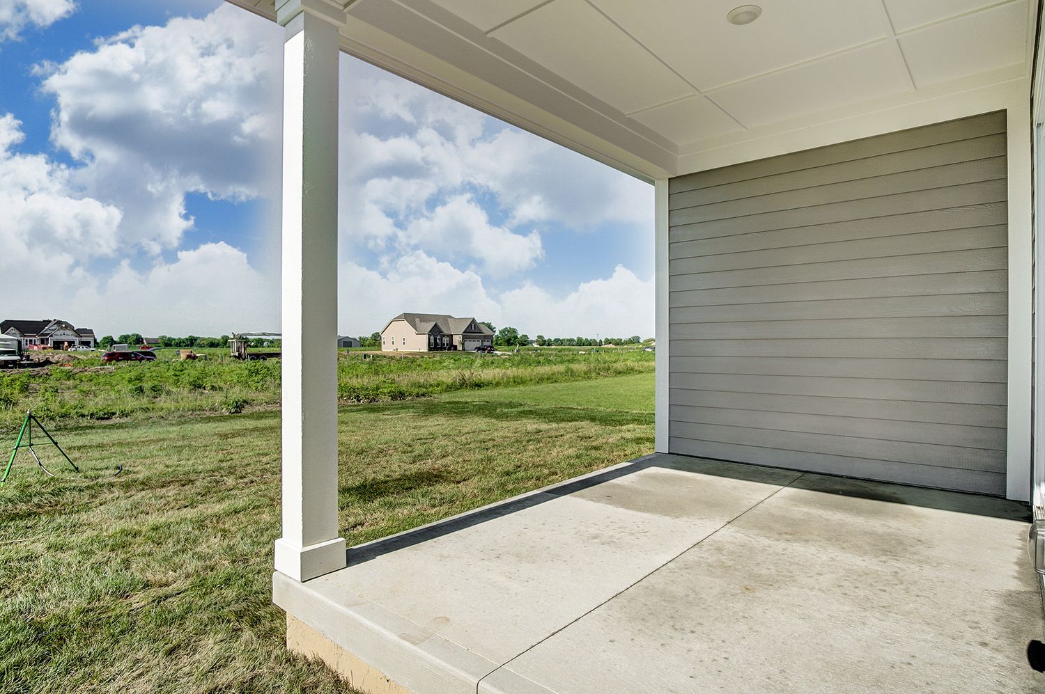 A porch with a view of a field and a house in the background.