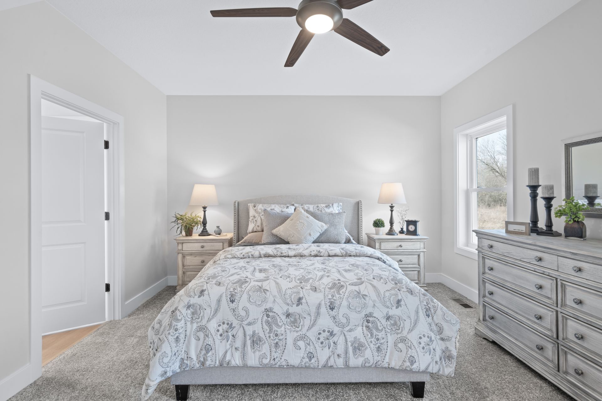 A bedroom with a bed , dresser , mirror and ceiling fan.