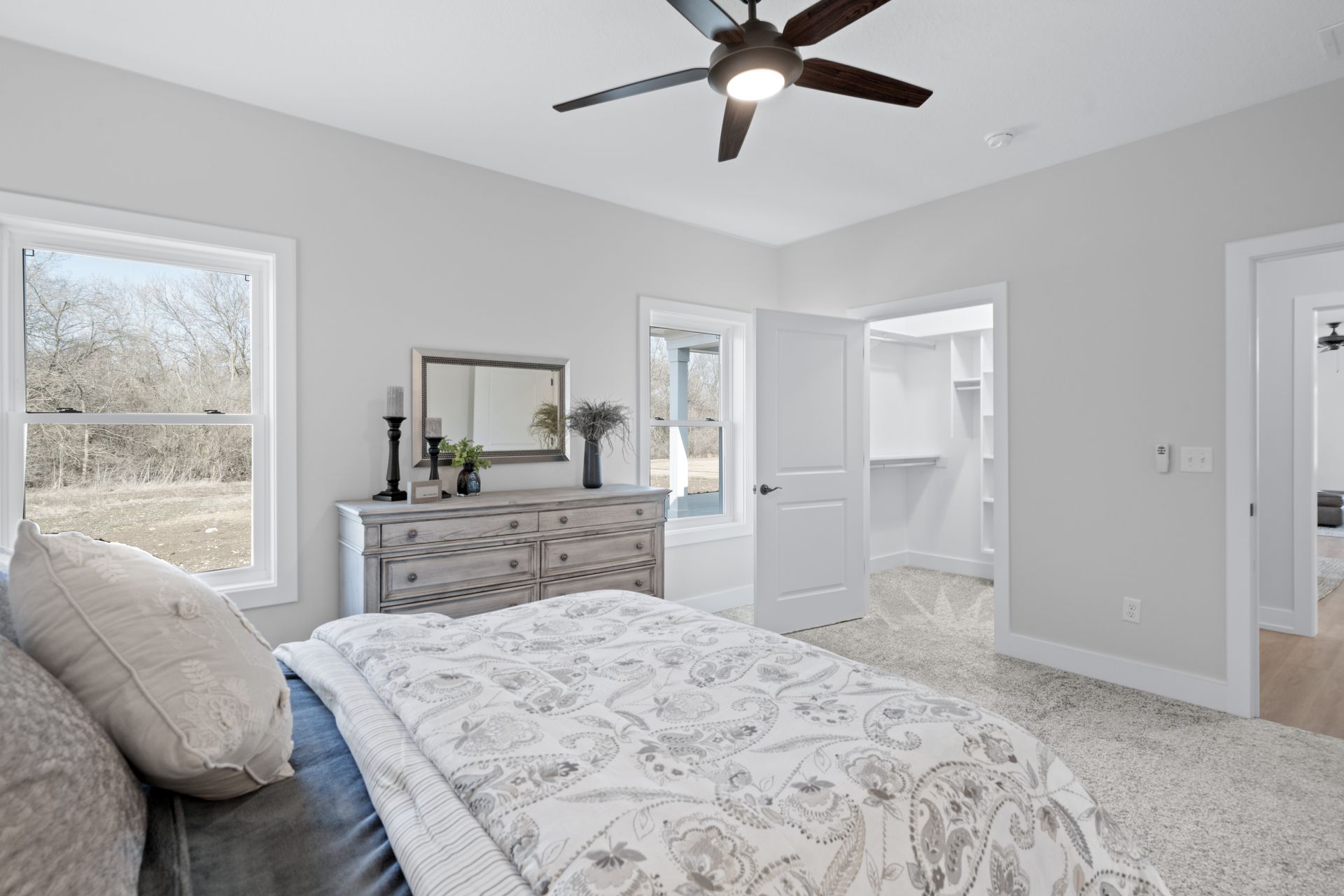 A bedroom with a bed , dresser , mirror and ceiling fan.