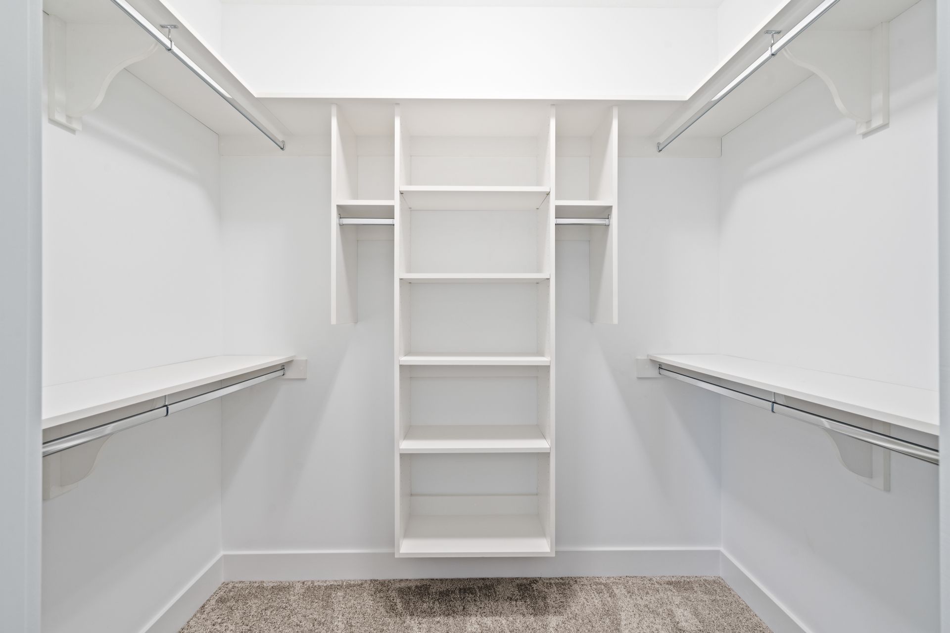 An empty walk in closet with white shelves and hanging racks.