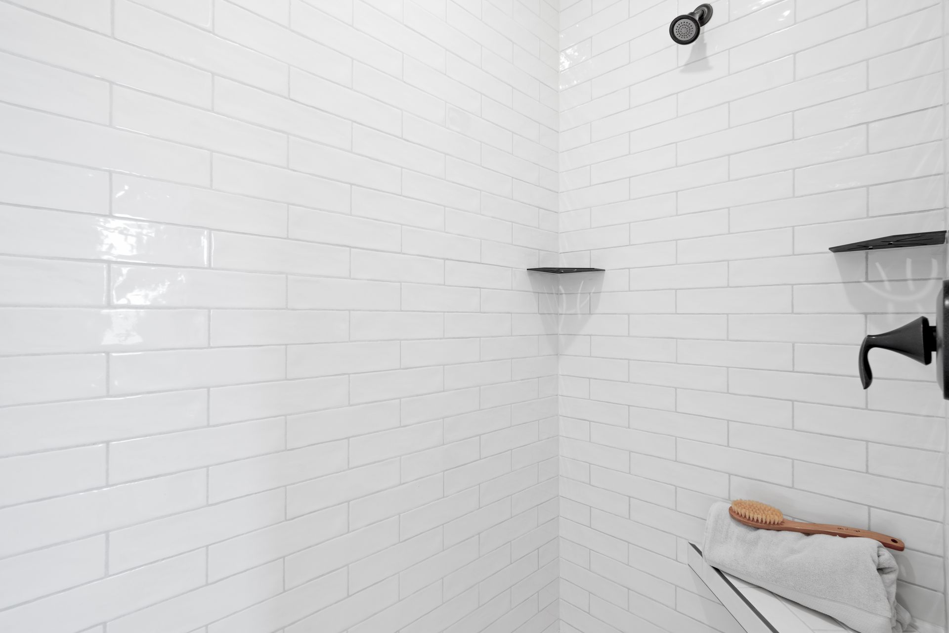 A bathroom with white tiles and a shower head.