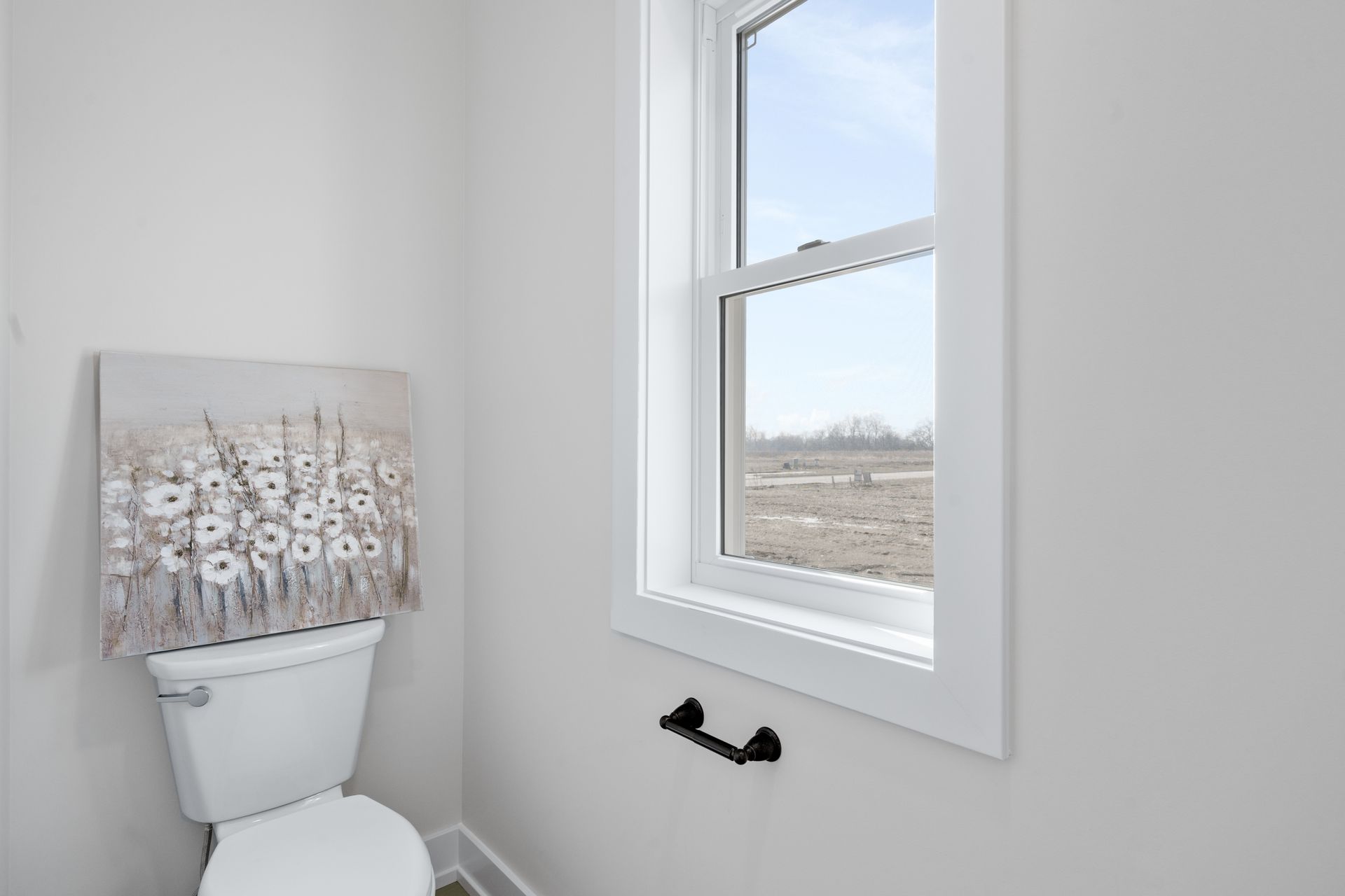 A bathroom with a toilet , window and a painting on the wall.