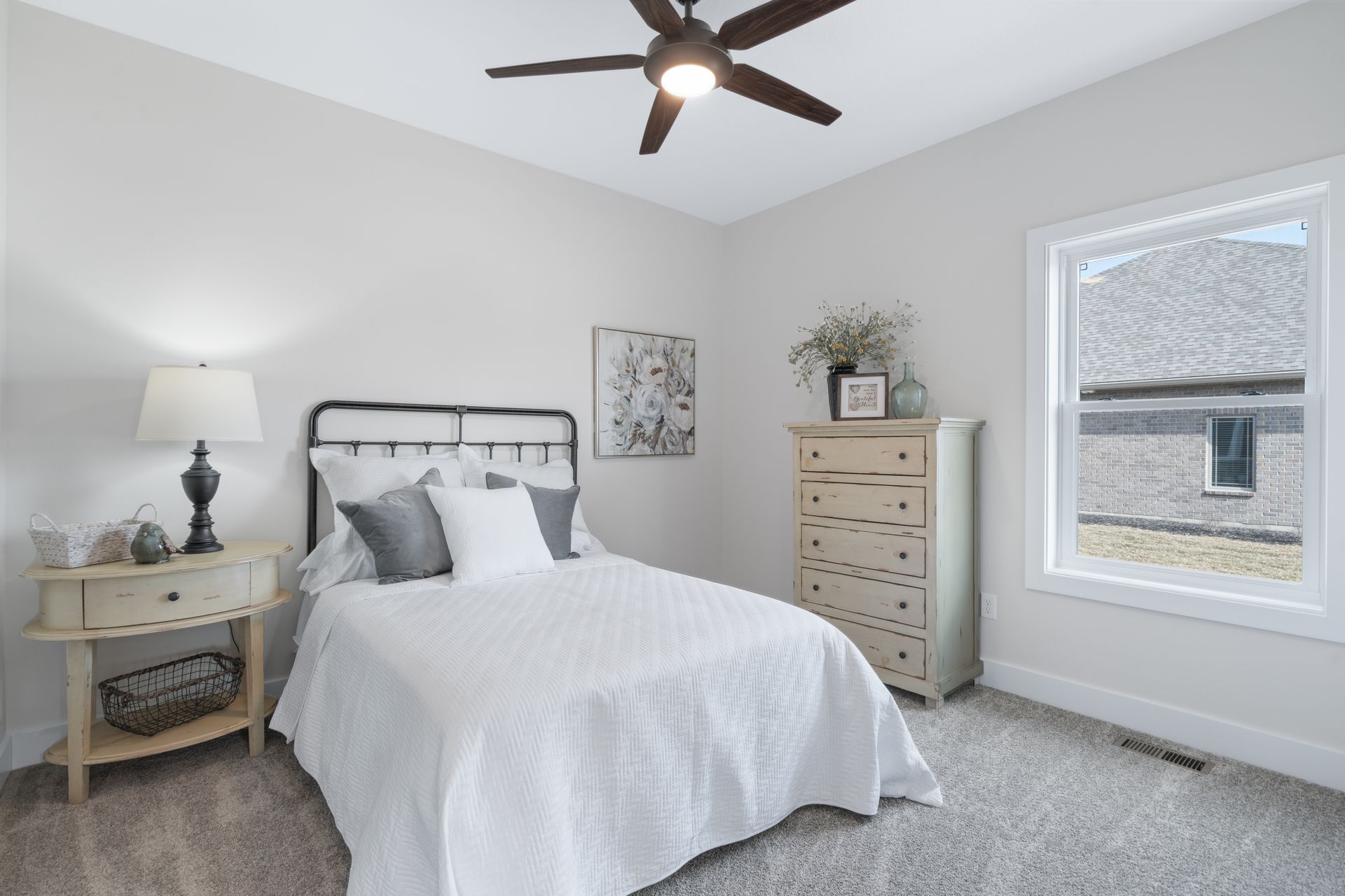 A bedroom with a bed , dresser , lamp and ceiling fan.