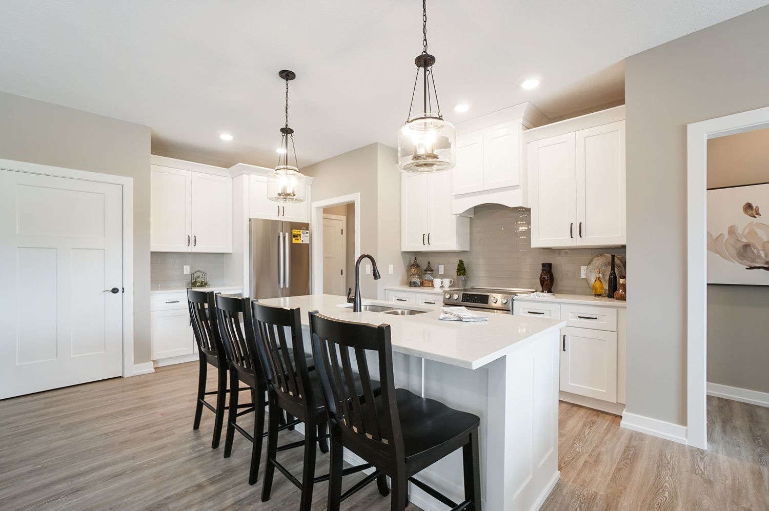 A kitchen with white cabinets and black chairs and a large island.