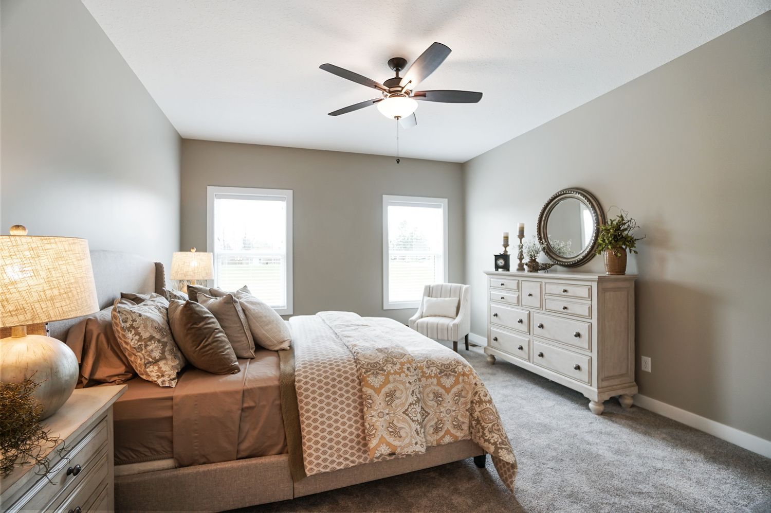 A bedroom with a bed , dresser , chair and ceiling fan.