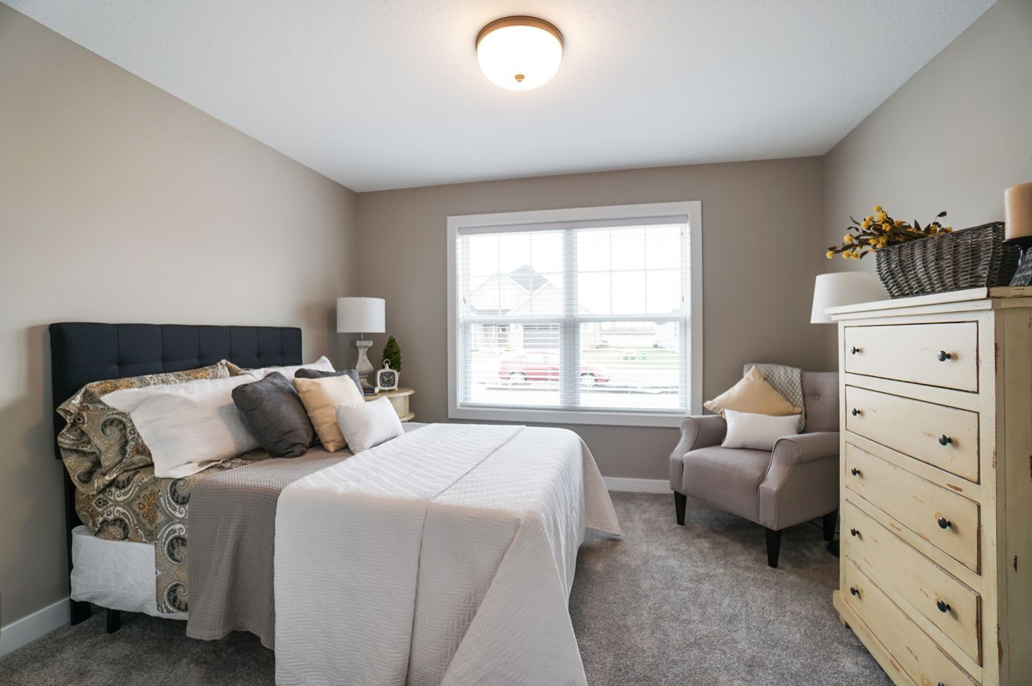 A bedroom with a bed , chair , dresser and window