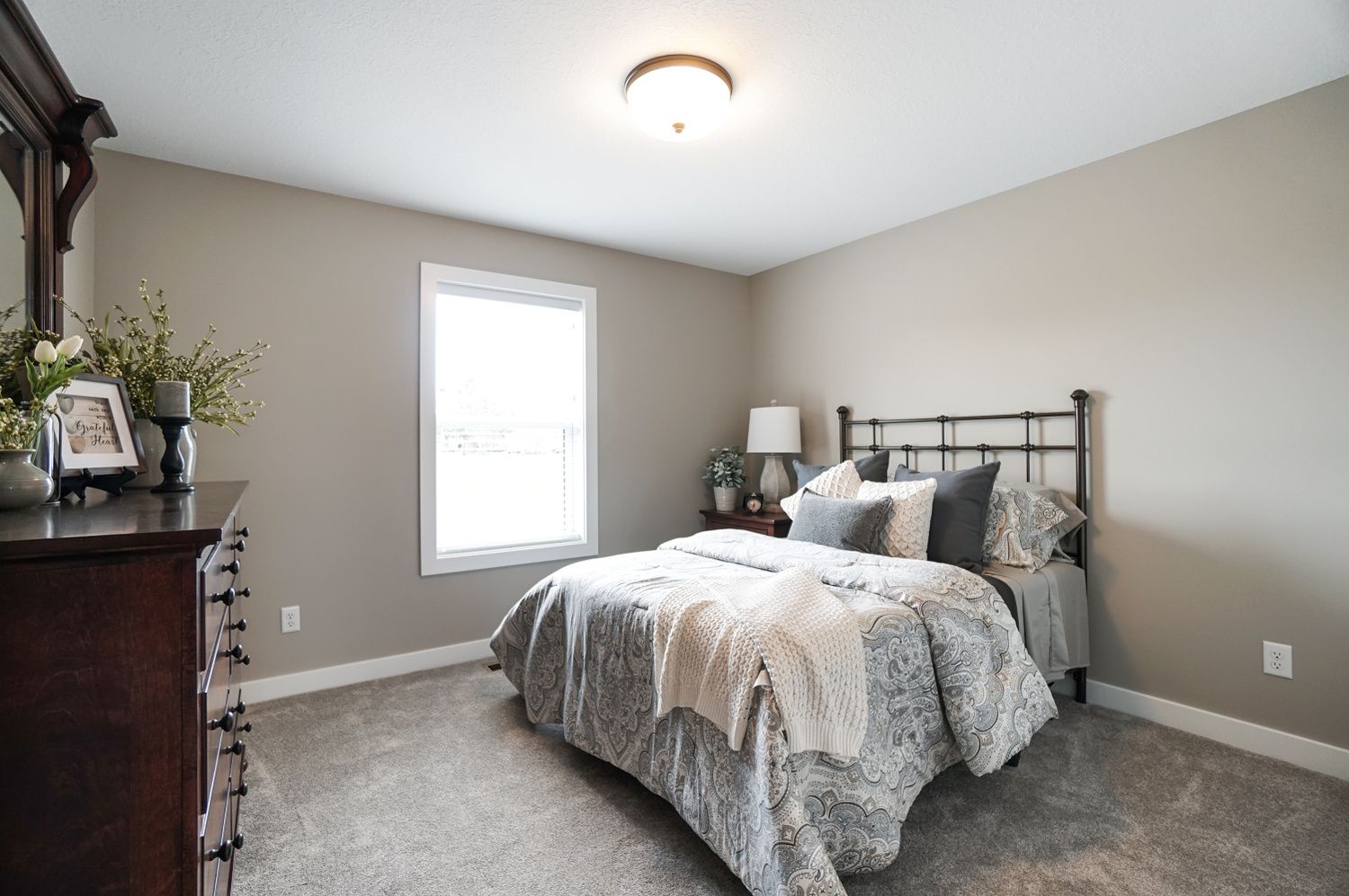A bedroom with a bed , dresser , mirror and window.