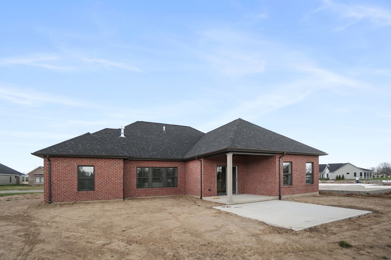 A brick house with a black roof is sitting on top of a dirt field.