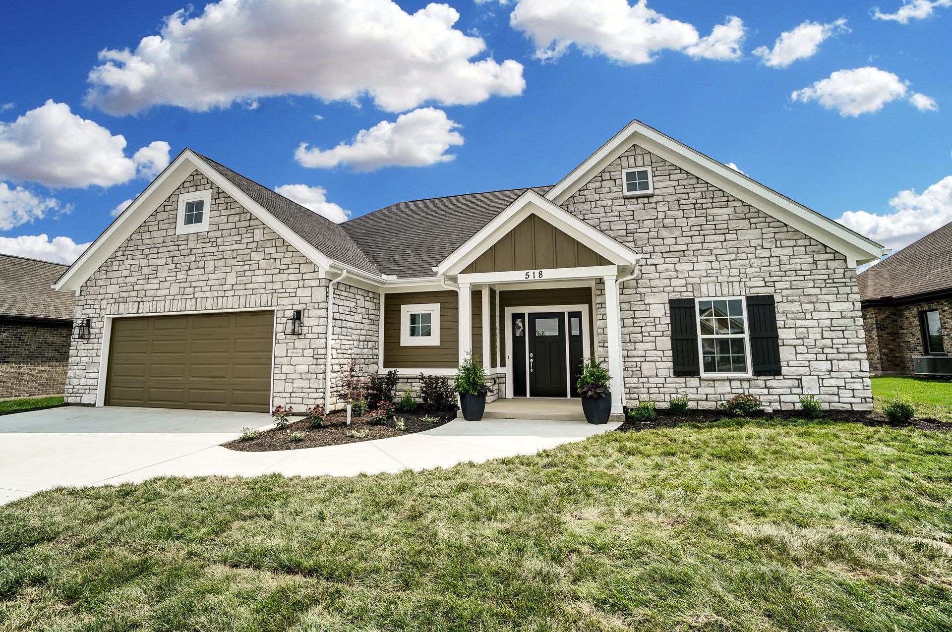 A large white brick house with a brown garage door is sitting on top of a lush green lawn.