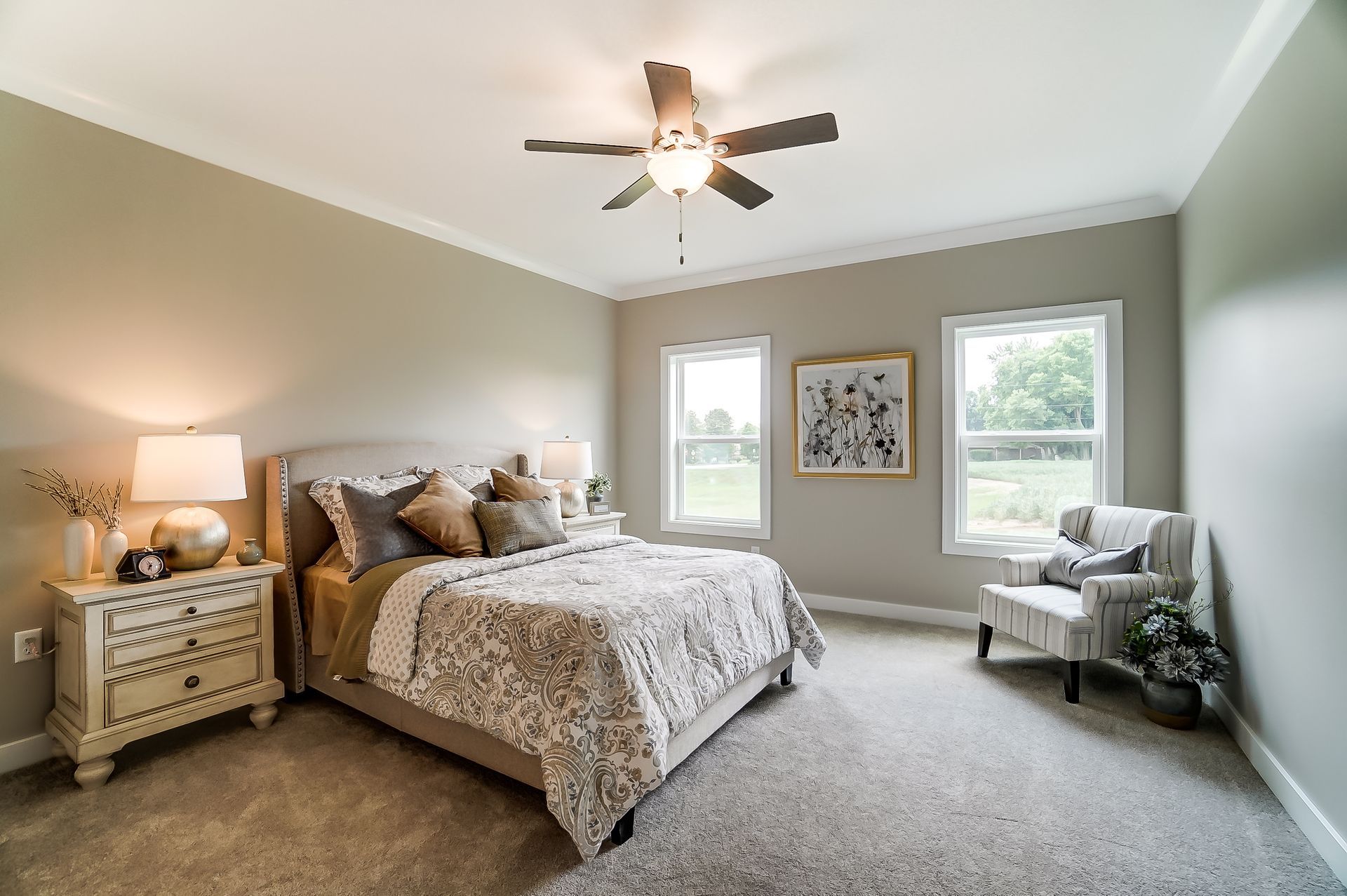 A bedroom with a bed , nightstand , chair and ceiling fan.