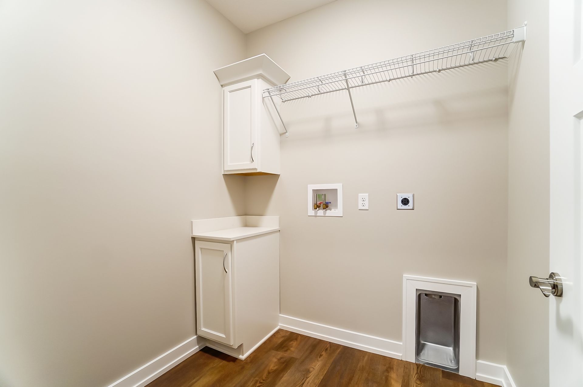 A laundry room with hardwood floors and white cabinets.