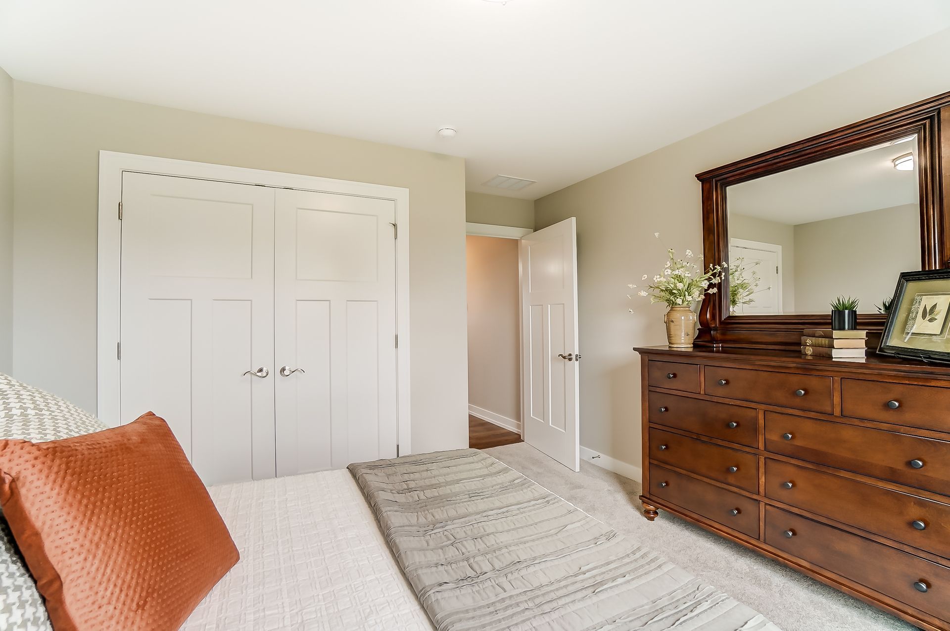 A bedroom with a bed , dresser , mirror and closet.