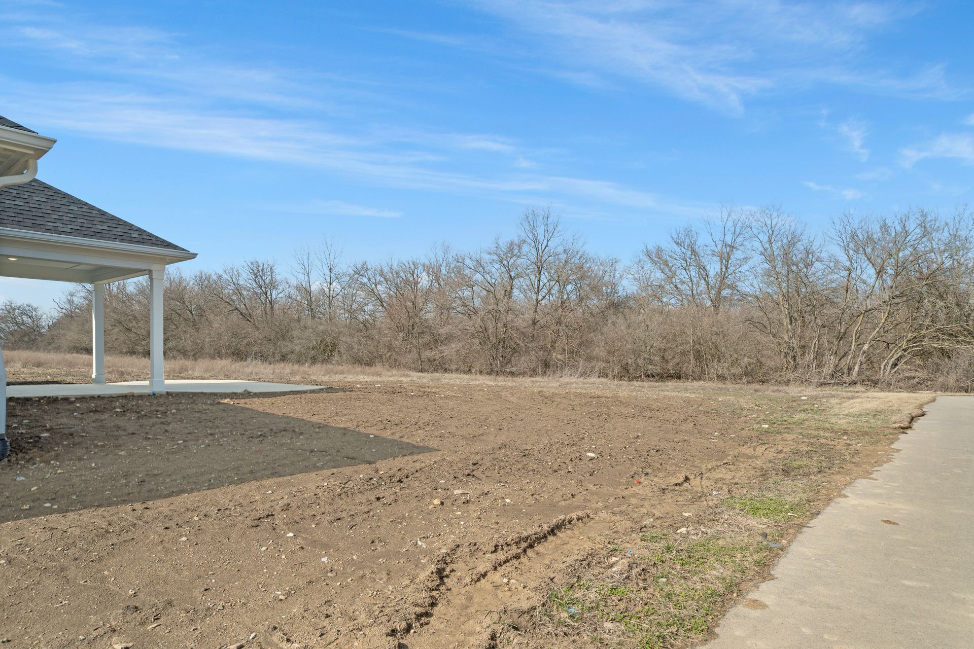 A house is sitting on top of a dirt field next to a road.