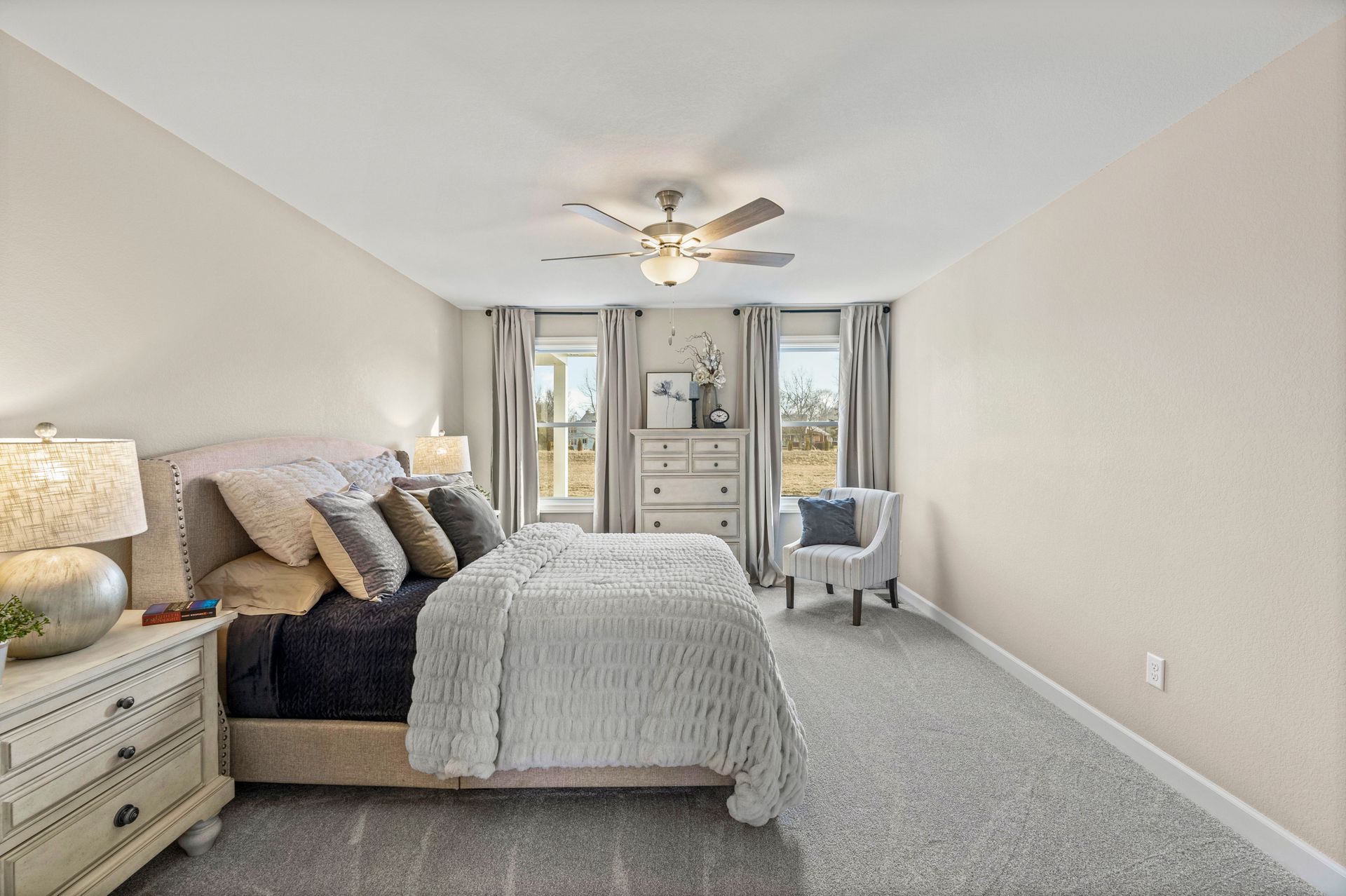 A bedroom with a bed , dresser , chair and ceiling fan.