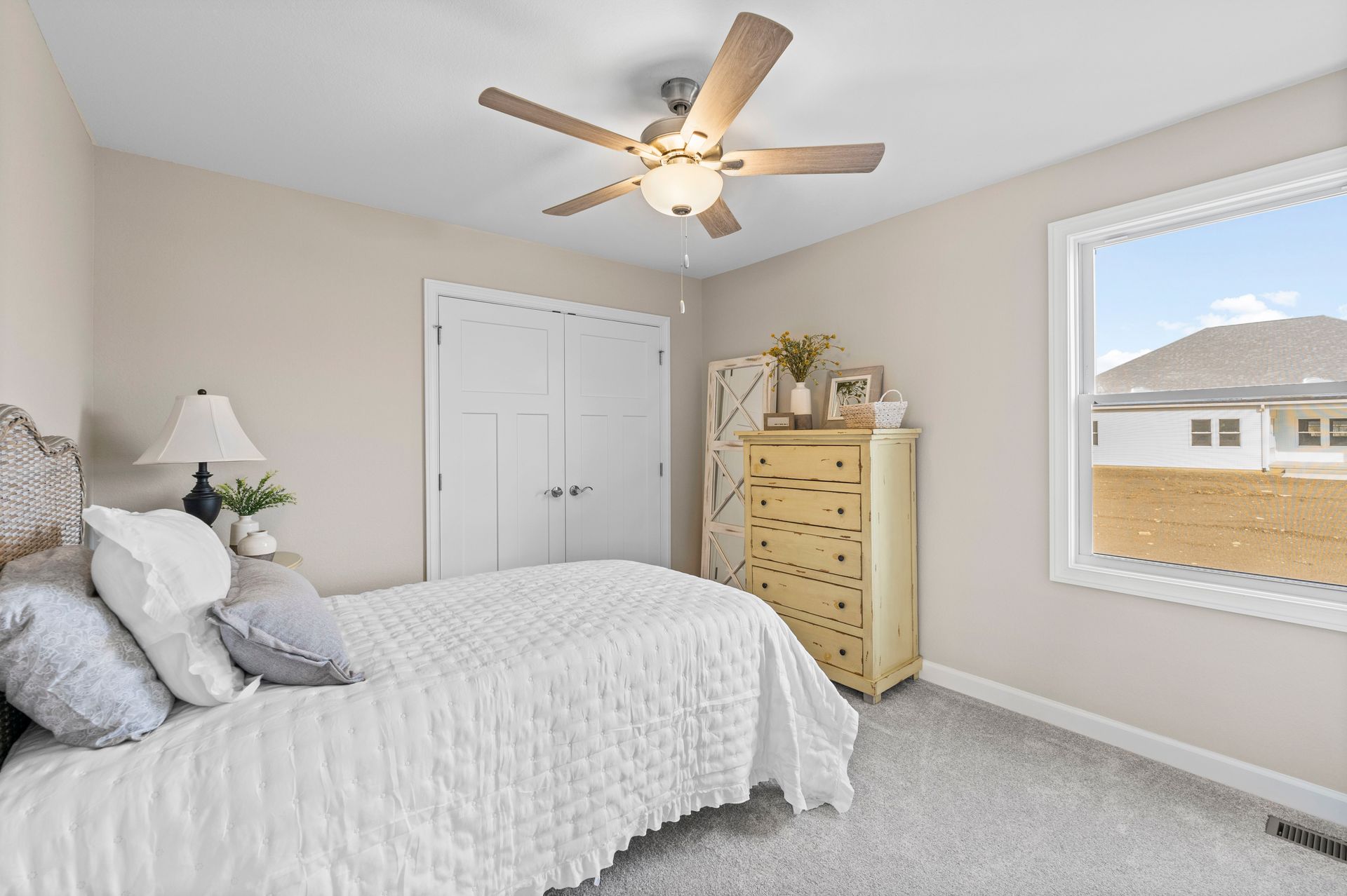 A bedroom with a bed , dresser , lamp and ceiling fan.