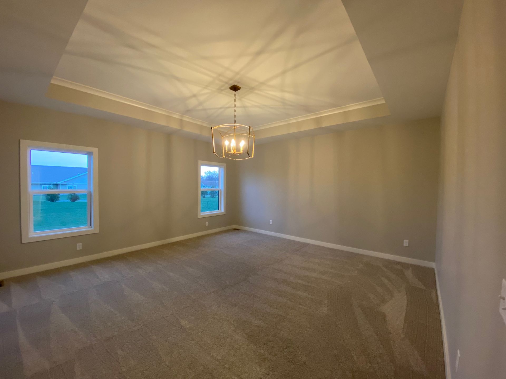 An empty room with a chandelier hanging from the ceiling and two windows.