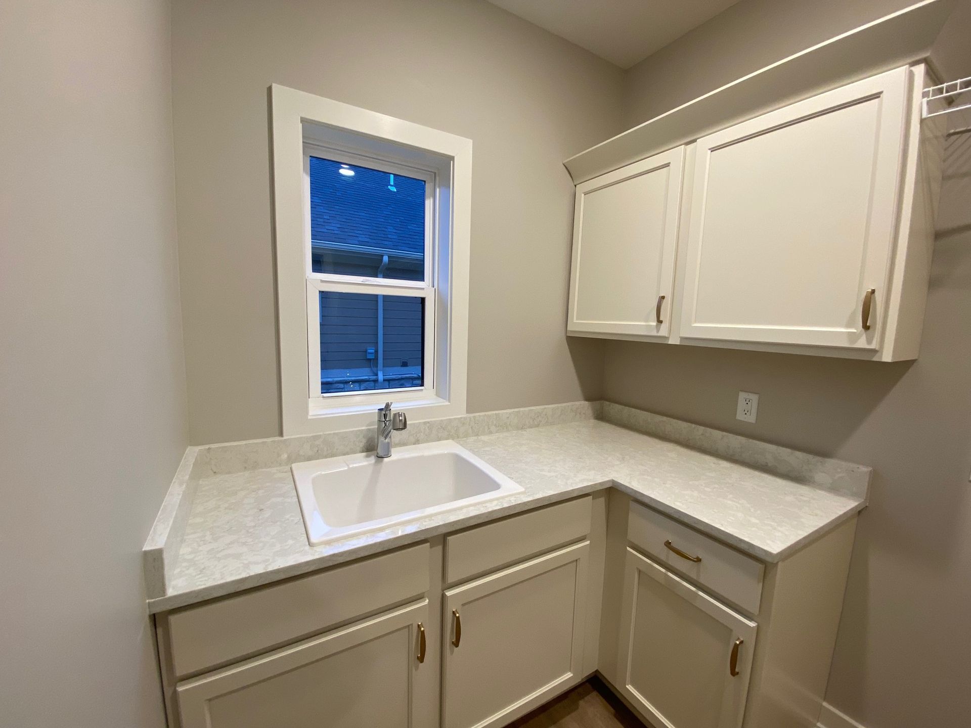 A laundry room with a sink , cabinets , and a window.