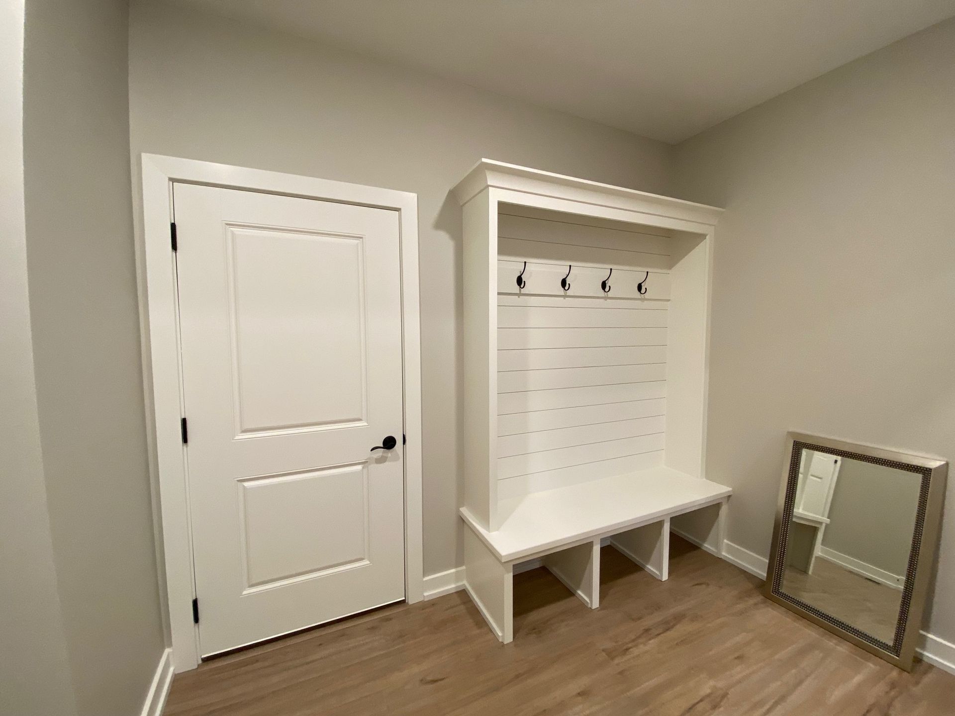 A hallway with a bench , coat rack , and mirror.