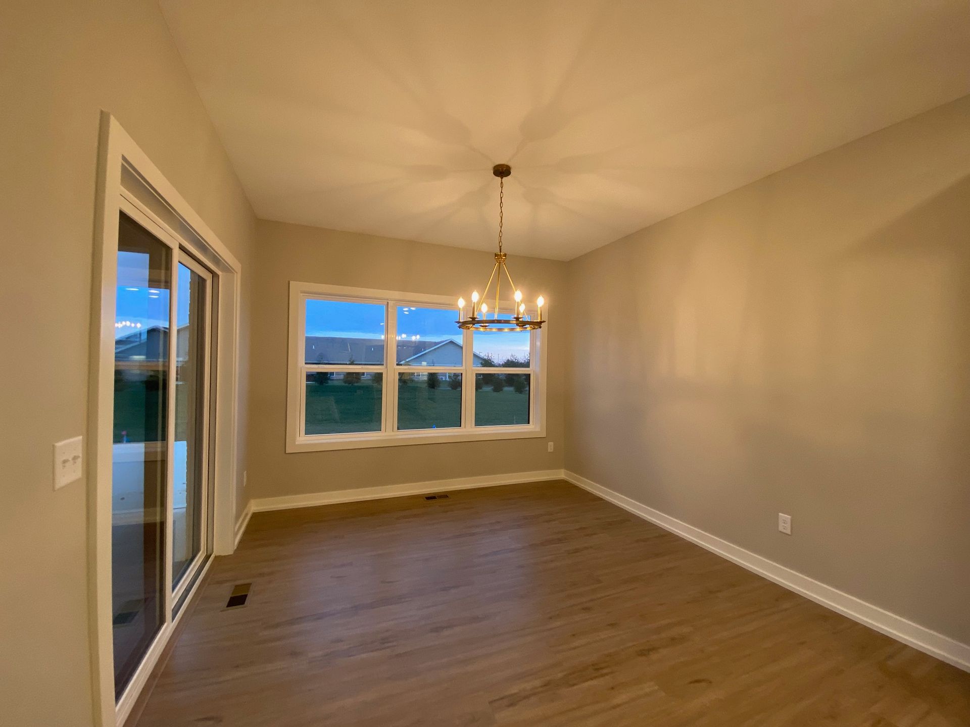 An empty living room with a chandelier and sliding glass doors.
