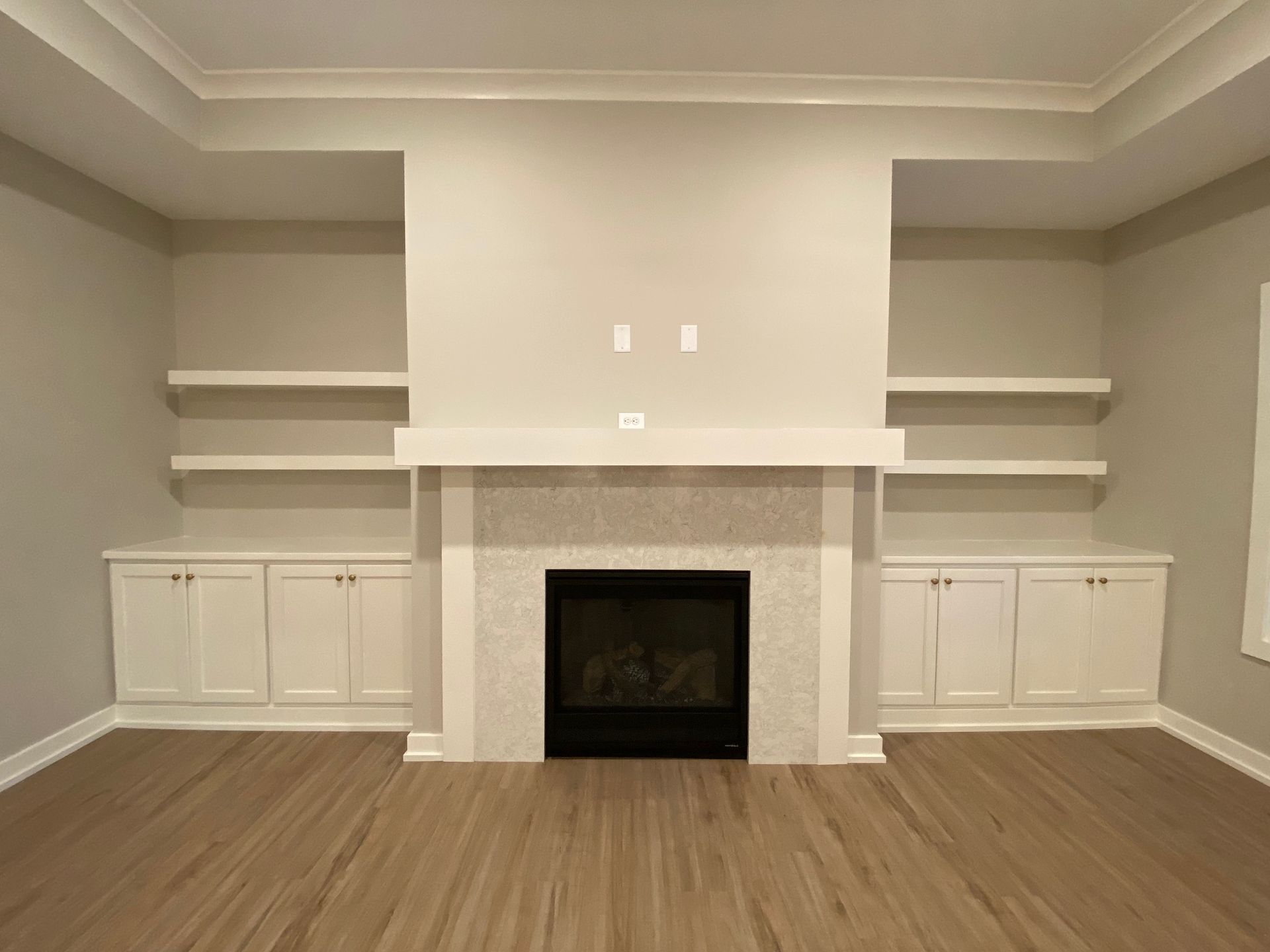 An empty living room with a fireplace and shelves.