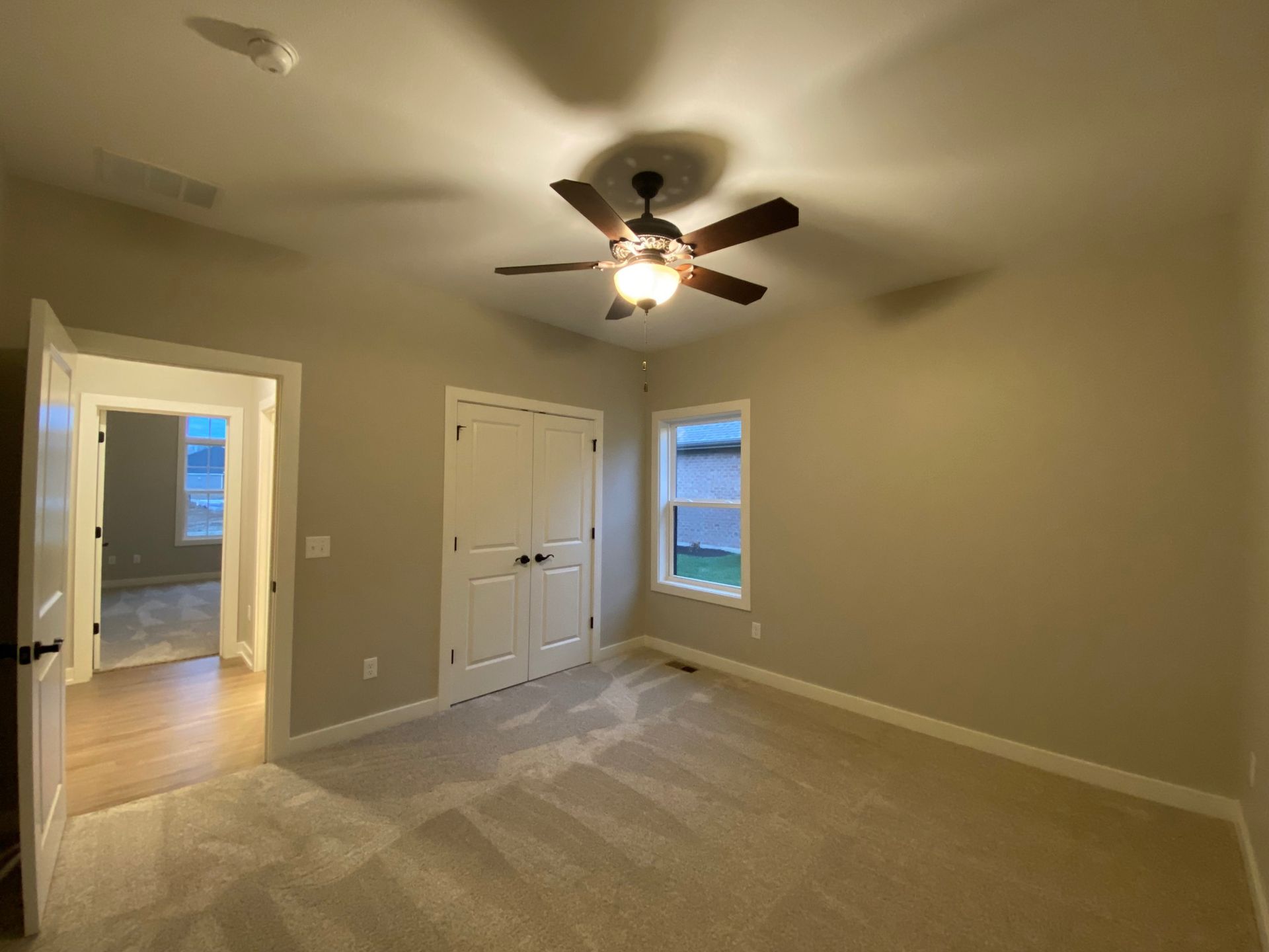 An empty bedroom with a ceiling fan and two windows.