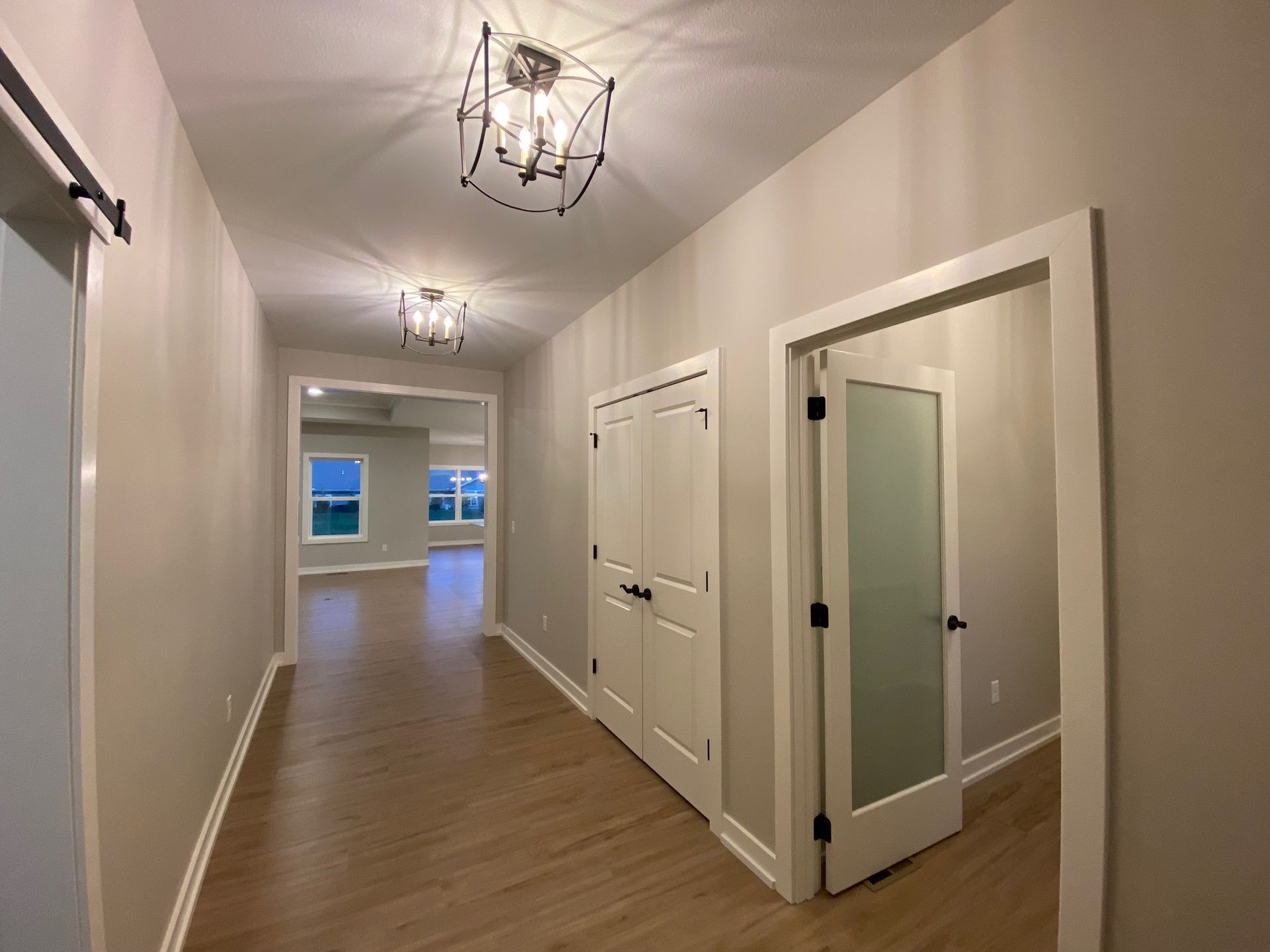 An empty hallway with hardwood floors and white doors leading to a living room.