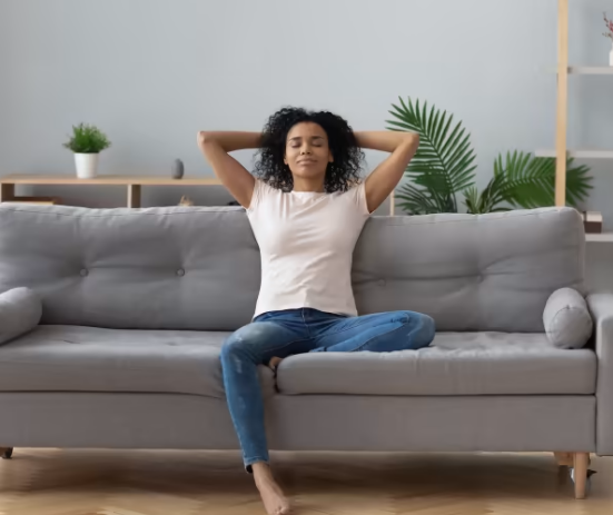 A woman is sitting on a couch with her hands behind her head.