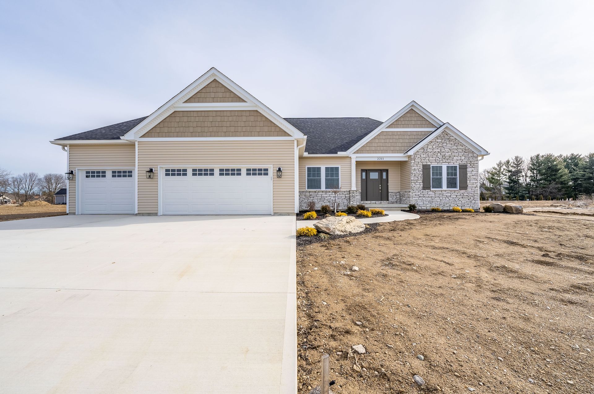 A house is sitting on top of a dirt field next to a concrete driveway.