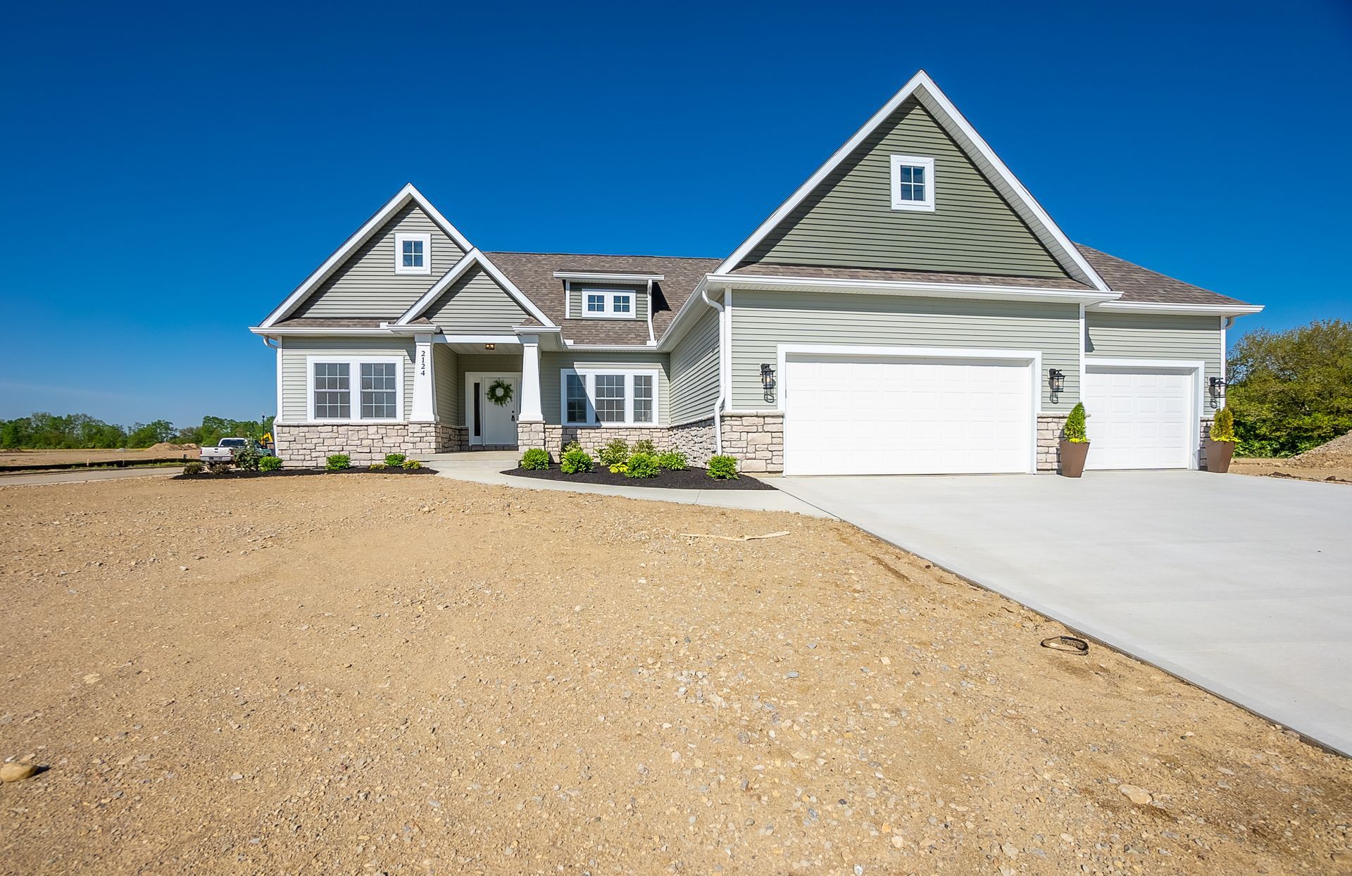 A large house with two garages is sitting on top of a dirt field.