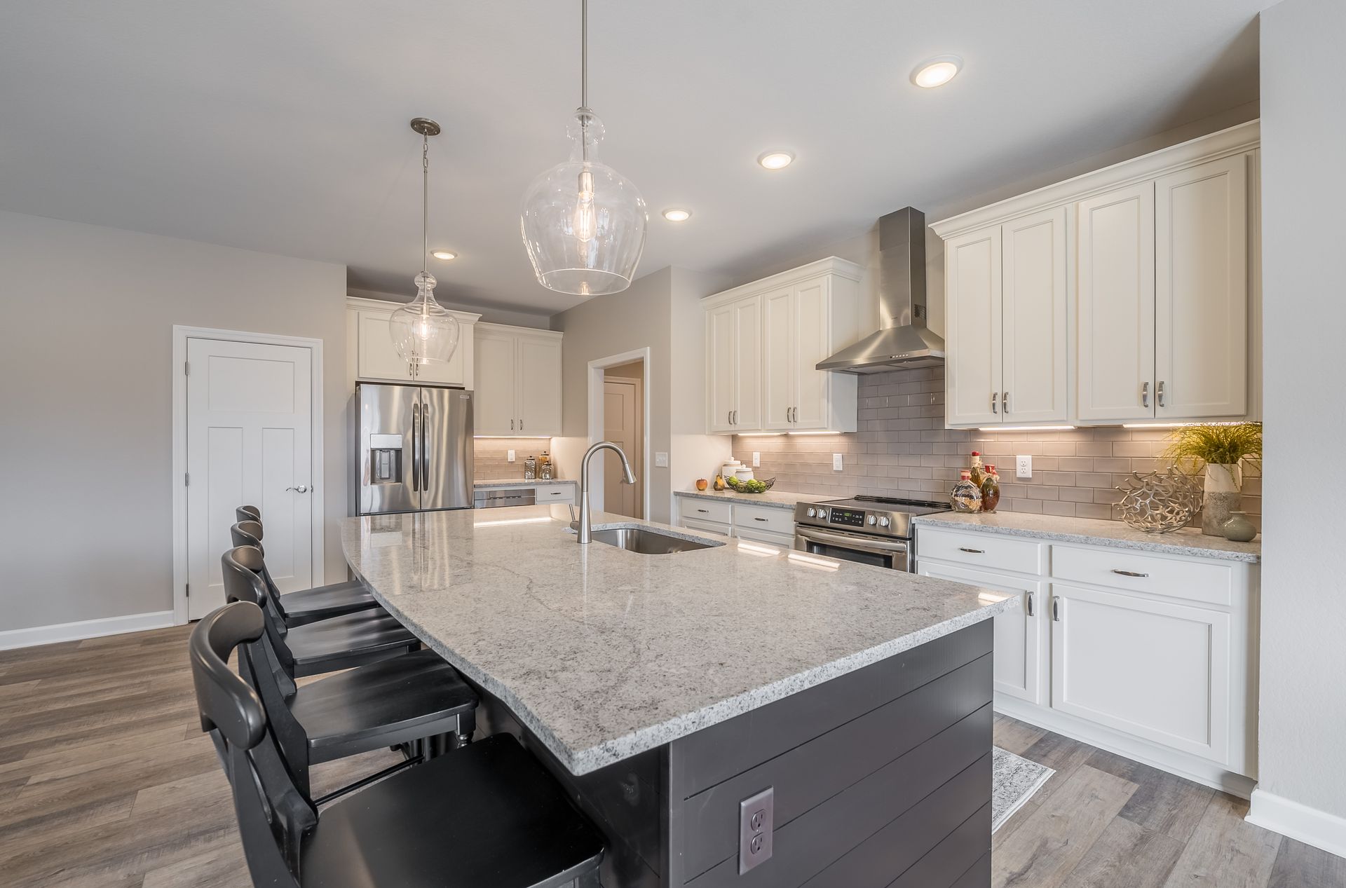 A kitchen with white cabinets , granite counter tops , stainless steel appliances and a large island.