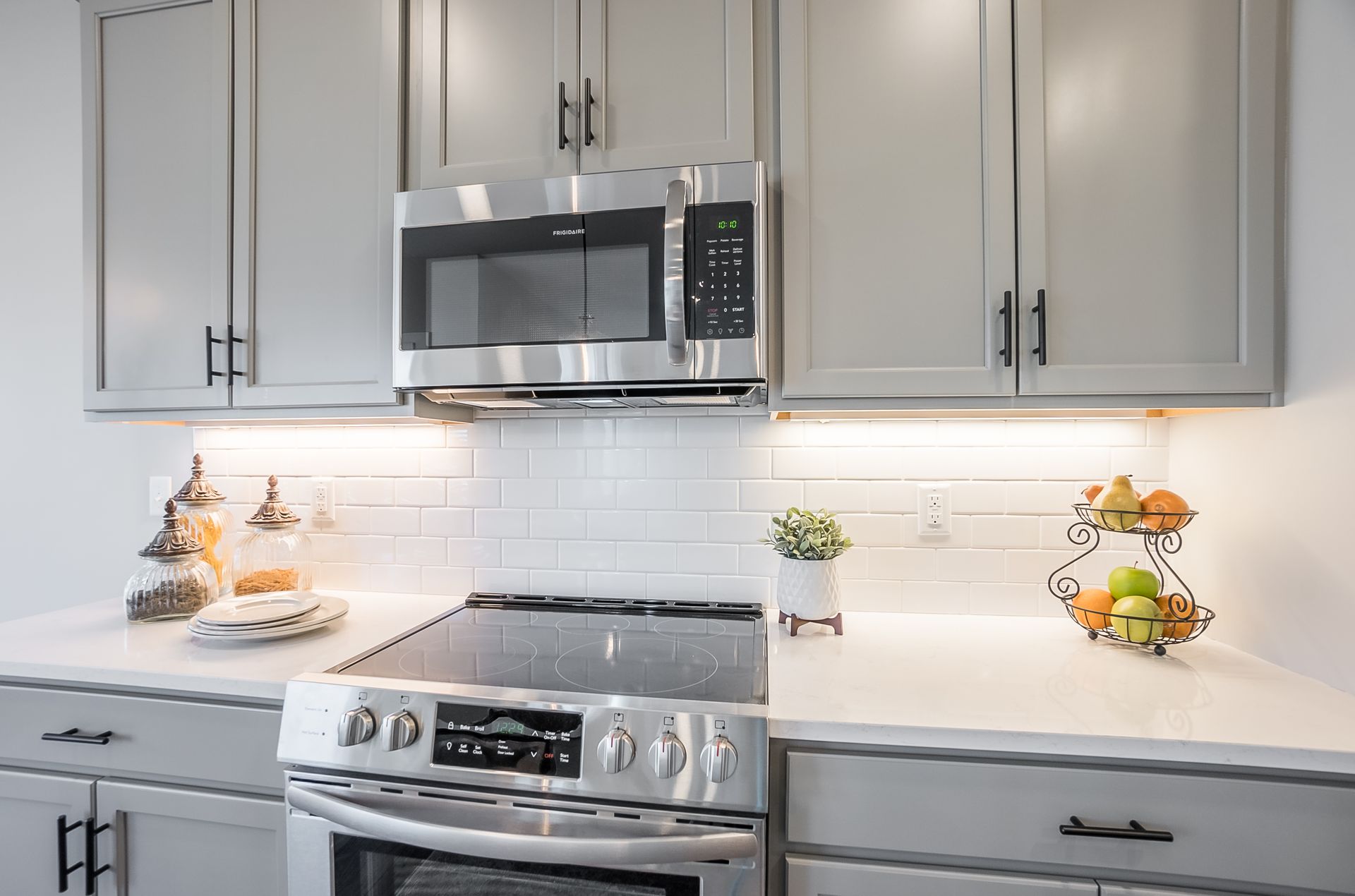 A kitchen with a stove , microwave , and gray cabinets.