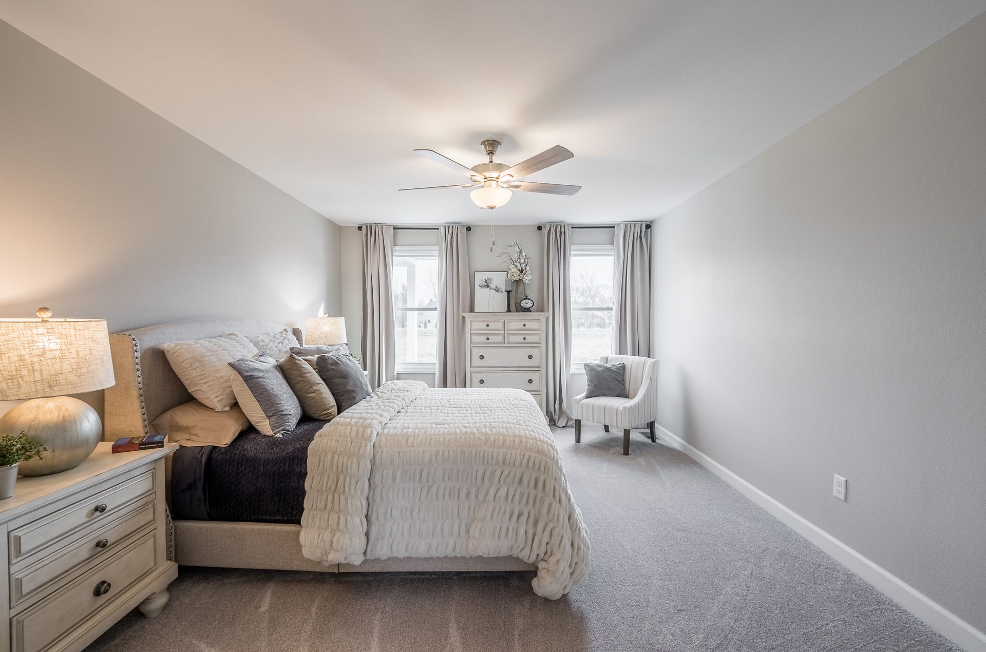 A bedroom with a bed , dresser , chair and ceiling fan.