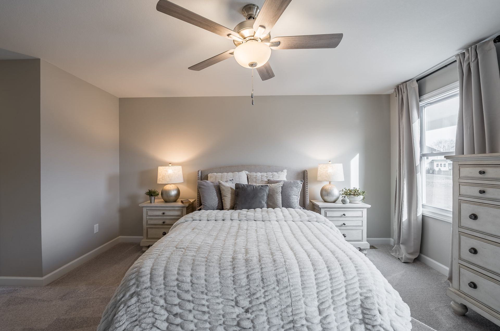 A bedroom with a bed , nightstand , dresser and ceiling fan.