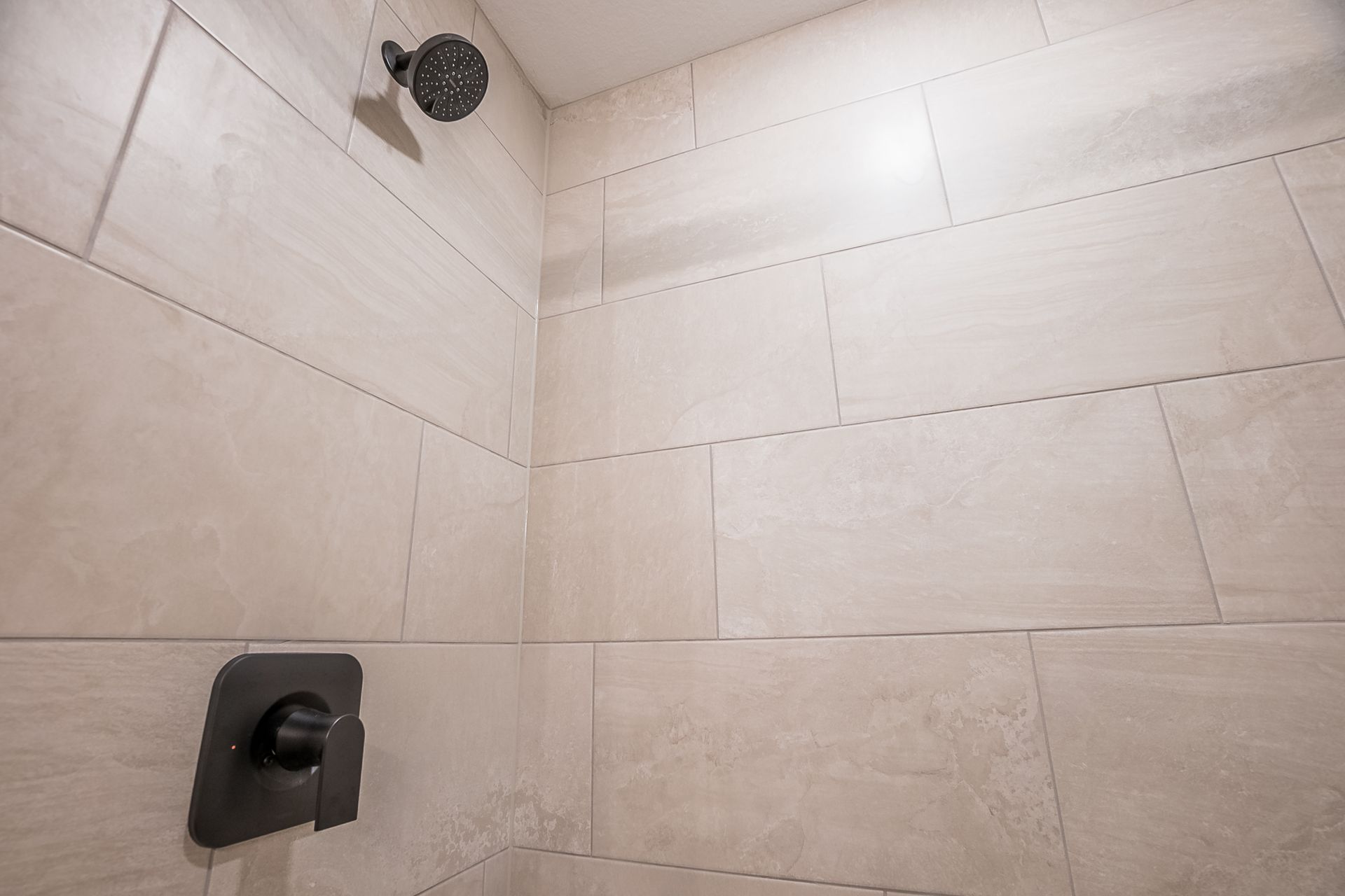 A shower with white tiles and a black shower head.