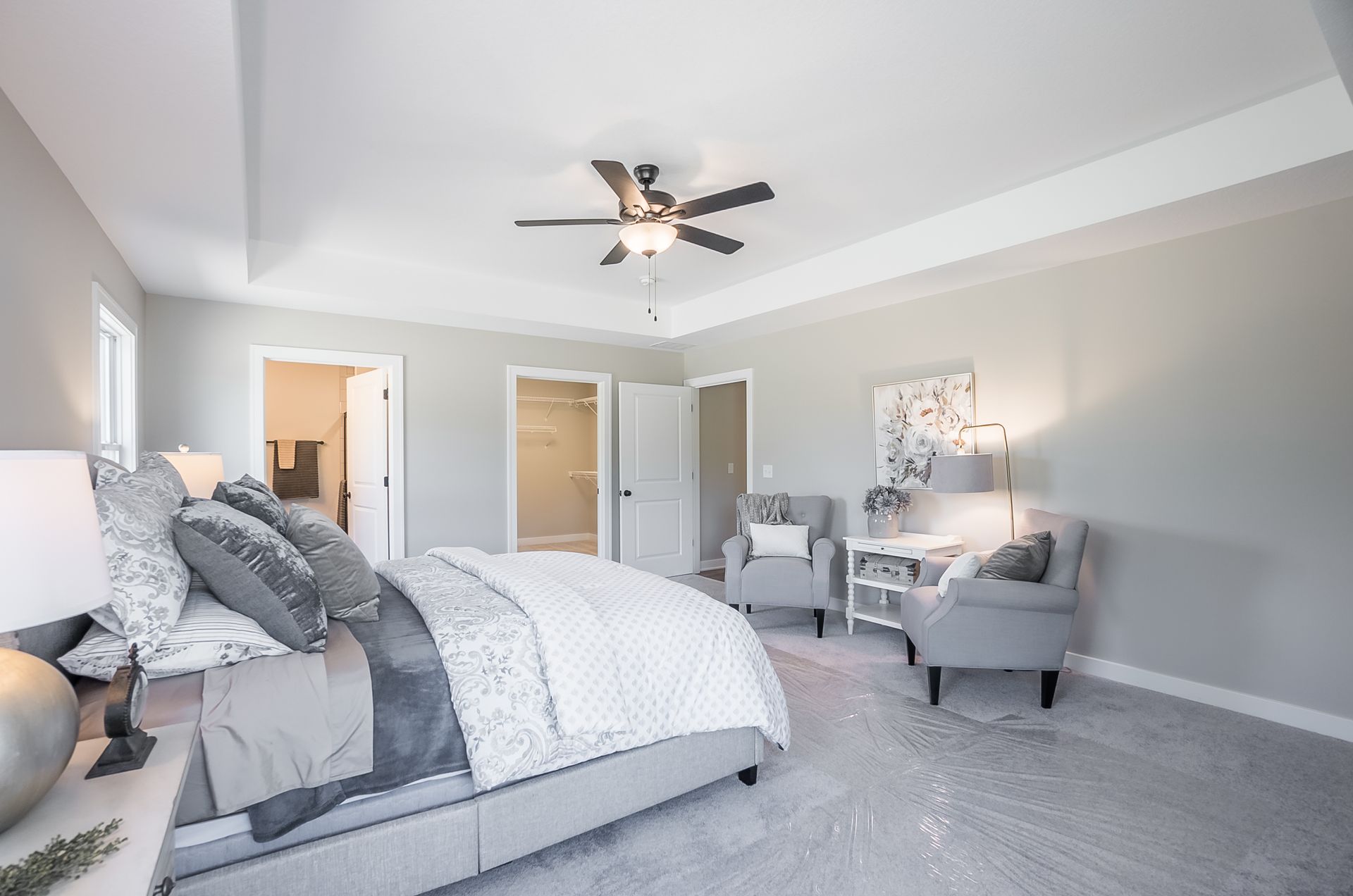 A bedroom with a bed , chairs , lamps and a ceiling fan.
