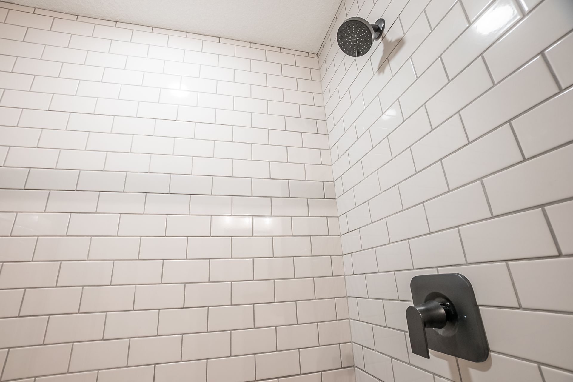 A shower with white tiles and a black shower head.