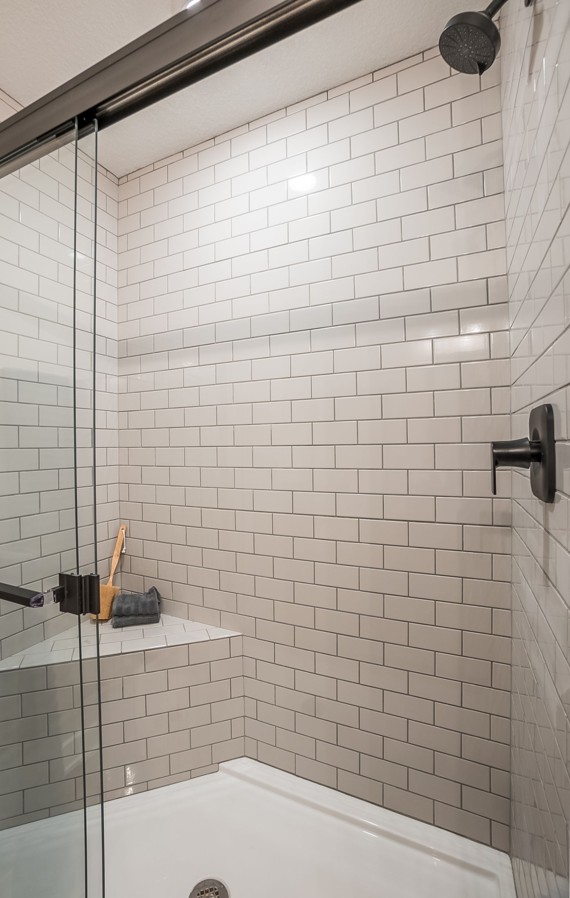 A bathroom with white tiles and a shower with a sliding glass door.