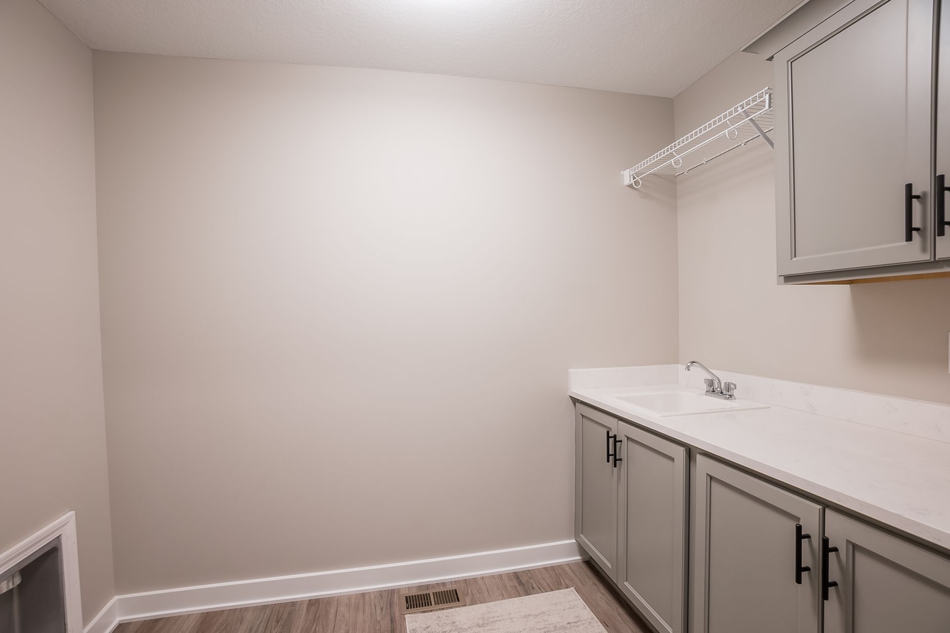 A laundry room with a sink , cabinets , and drying rack.