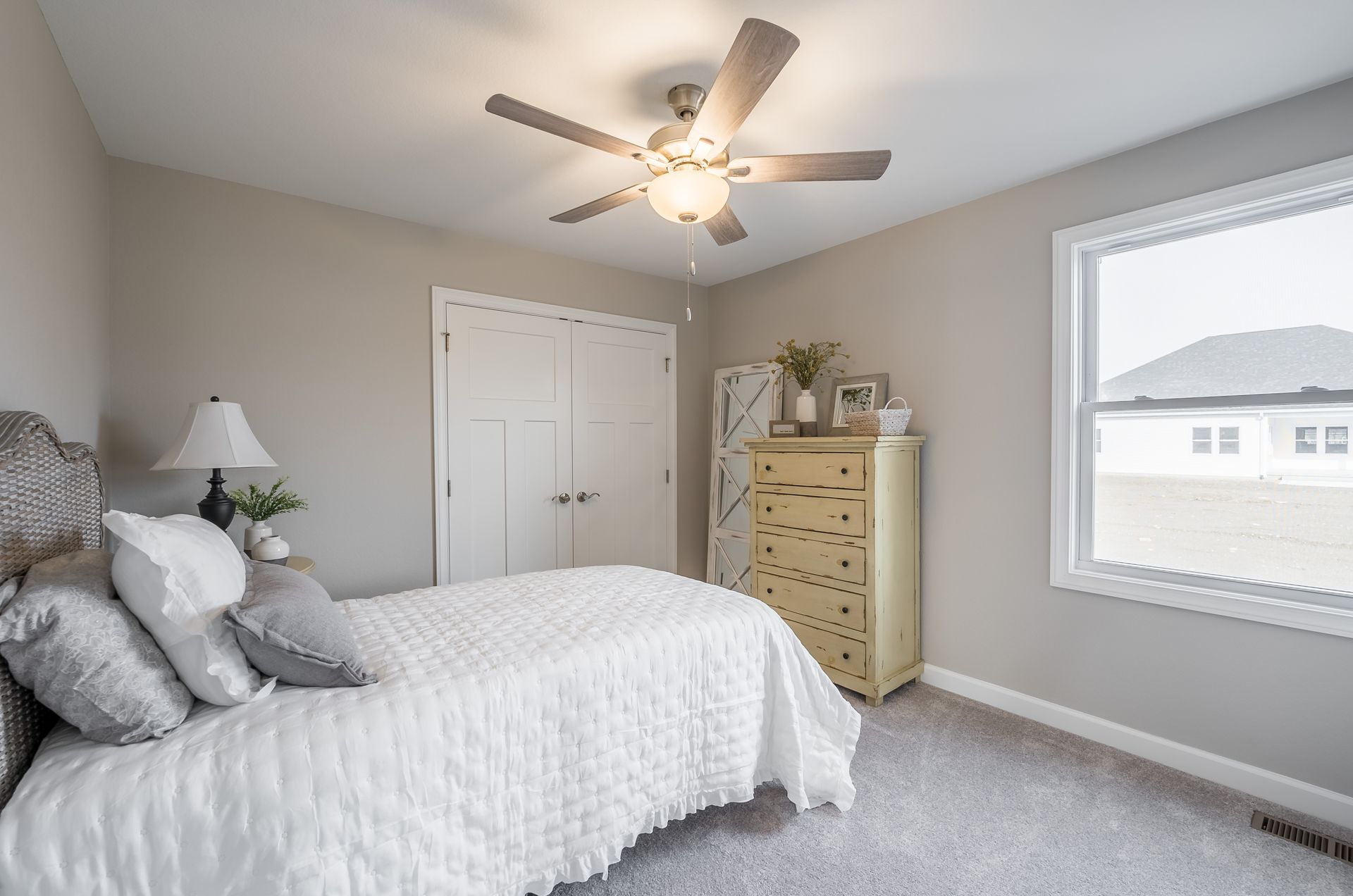 A bedroom with a bed , dresser , lamp and ceiling fan.