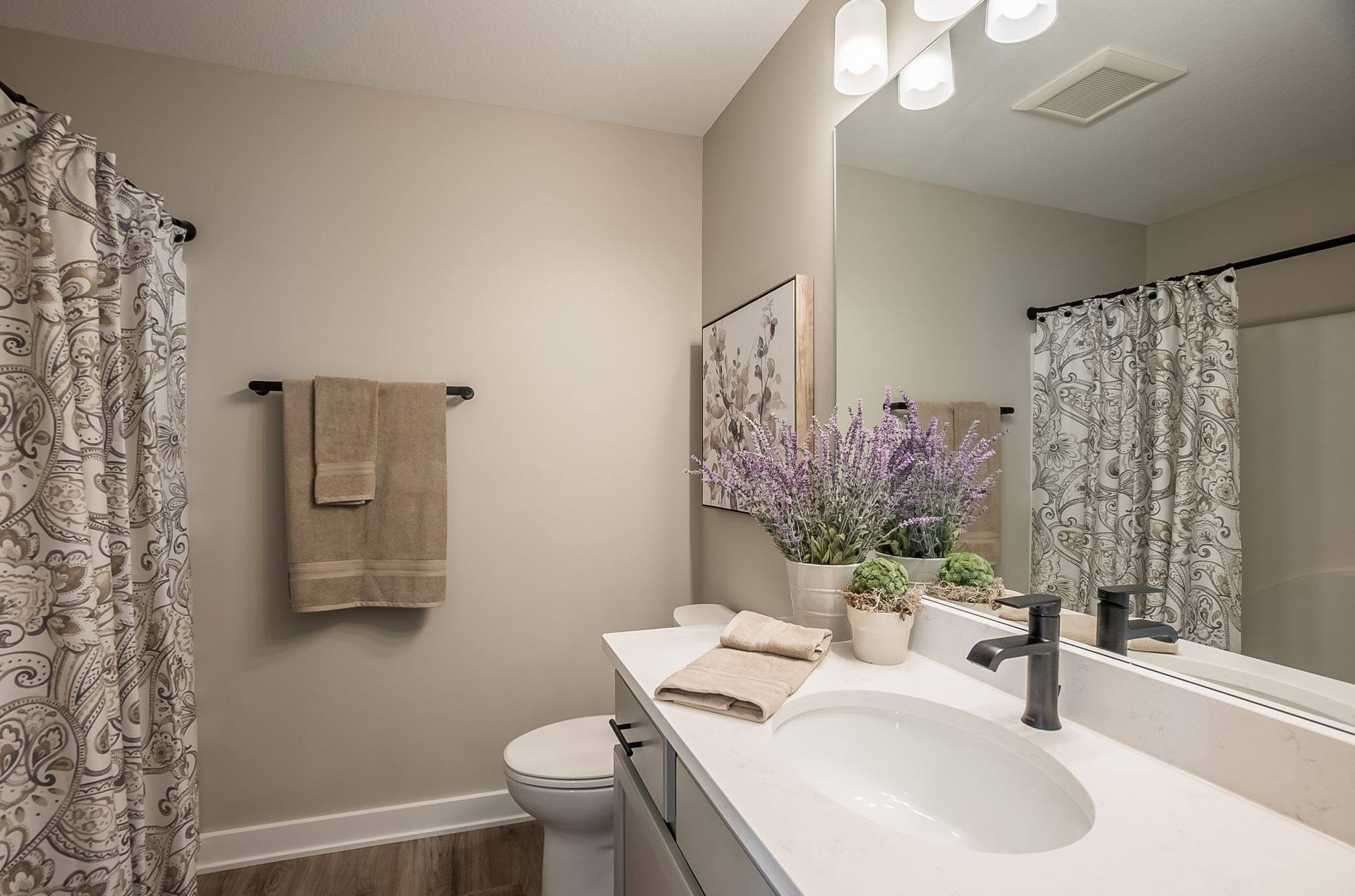 A bathroom with a sink , toilet , shower curtain and mirror.